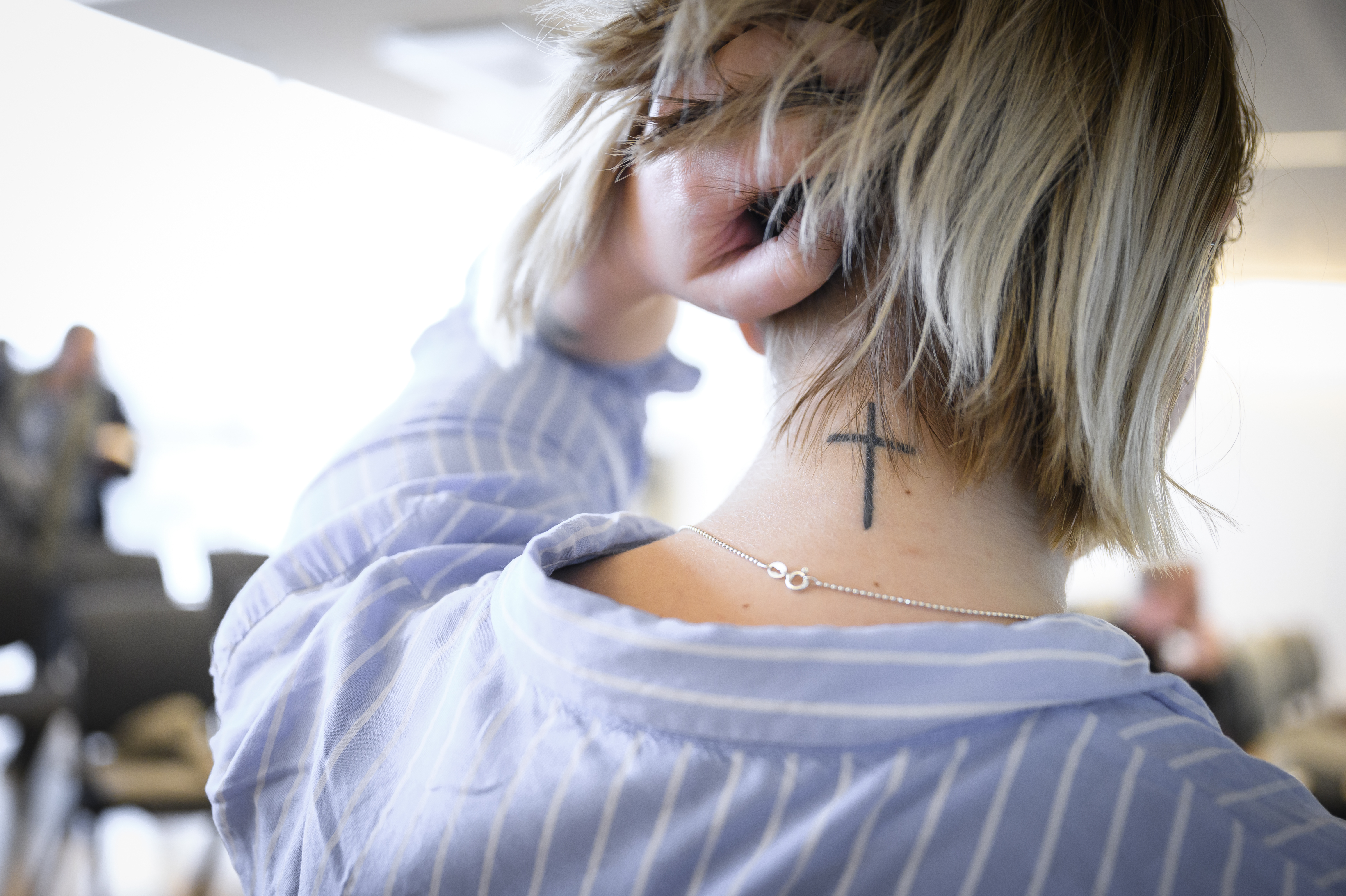 En kvinna lyfter upp sitt blonda hår i nacken för att visa en tatuering som föreställer ett kors.