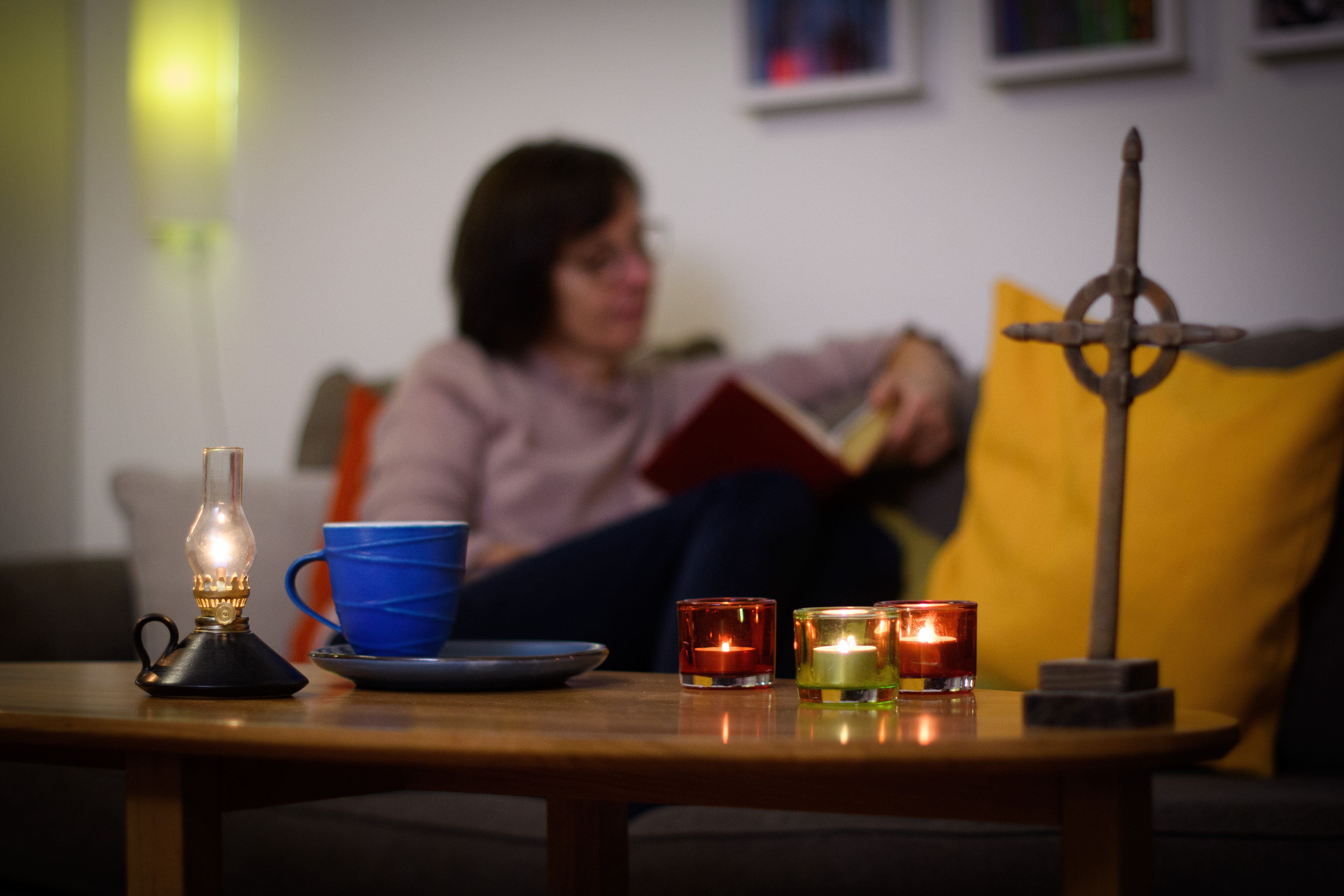 En kvinna läser hemma i soffan. På soffbordet framför henne står tända ljus och ett kors.