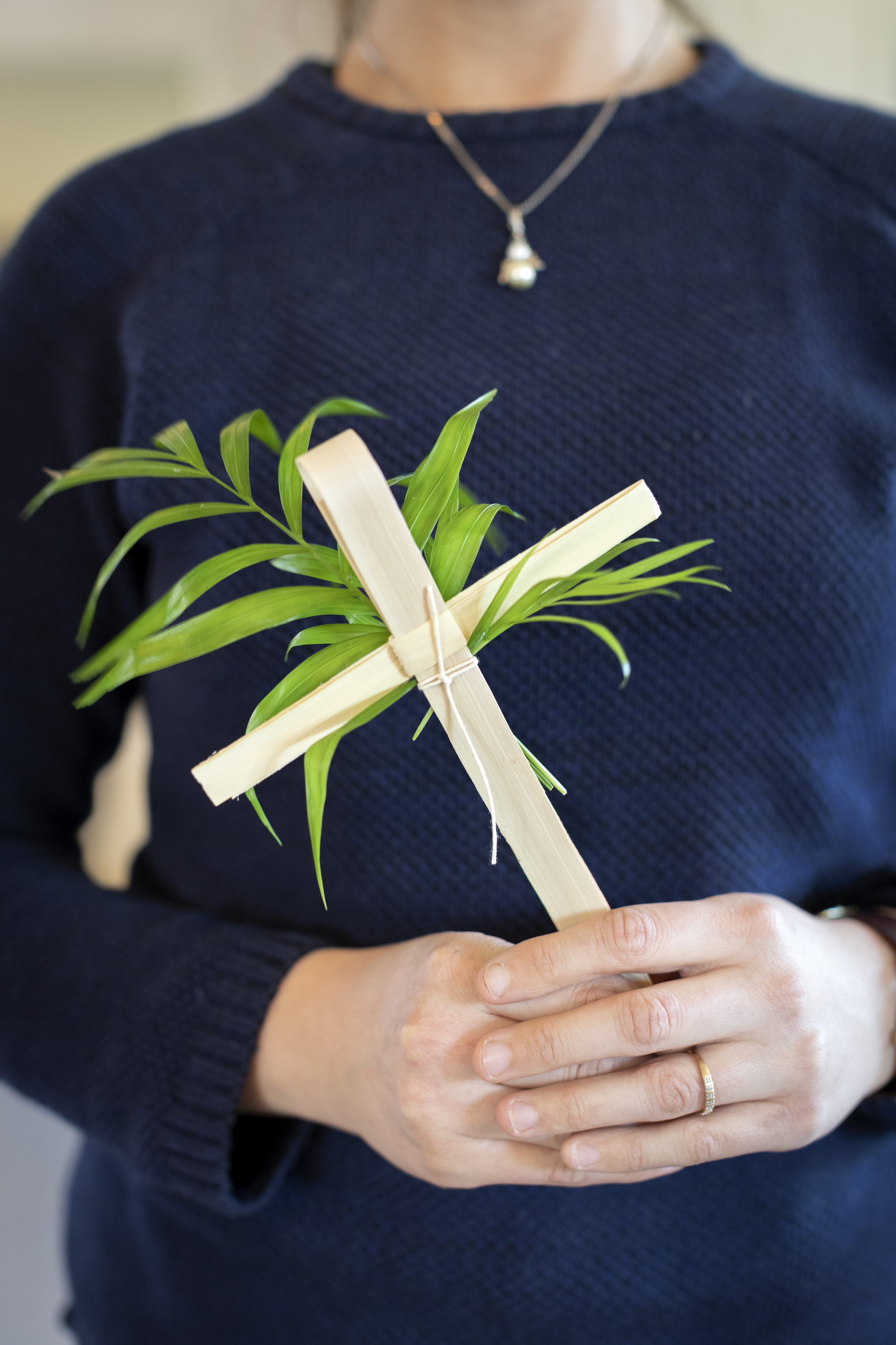 Någon håller ett träkors med fastknutna palmblad.