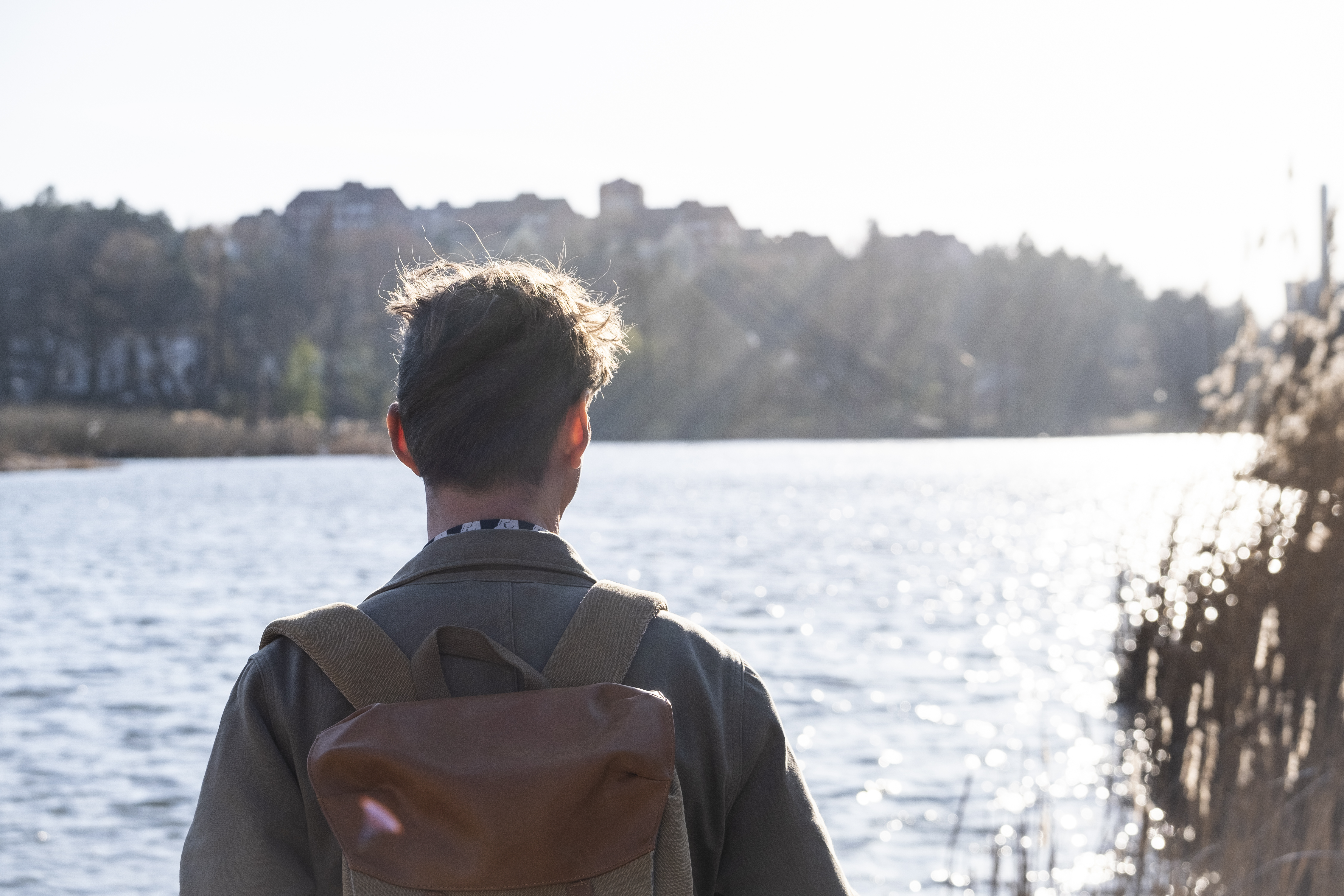 En man med ryggsäck tittar ut över vattnet i solen.