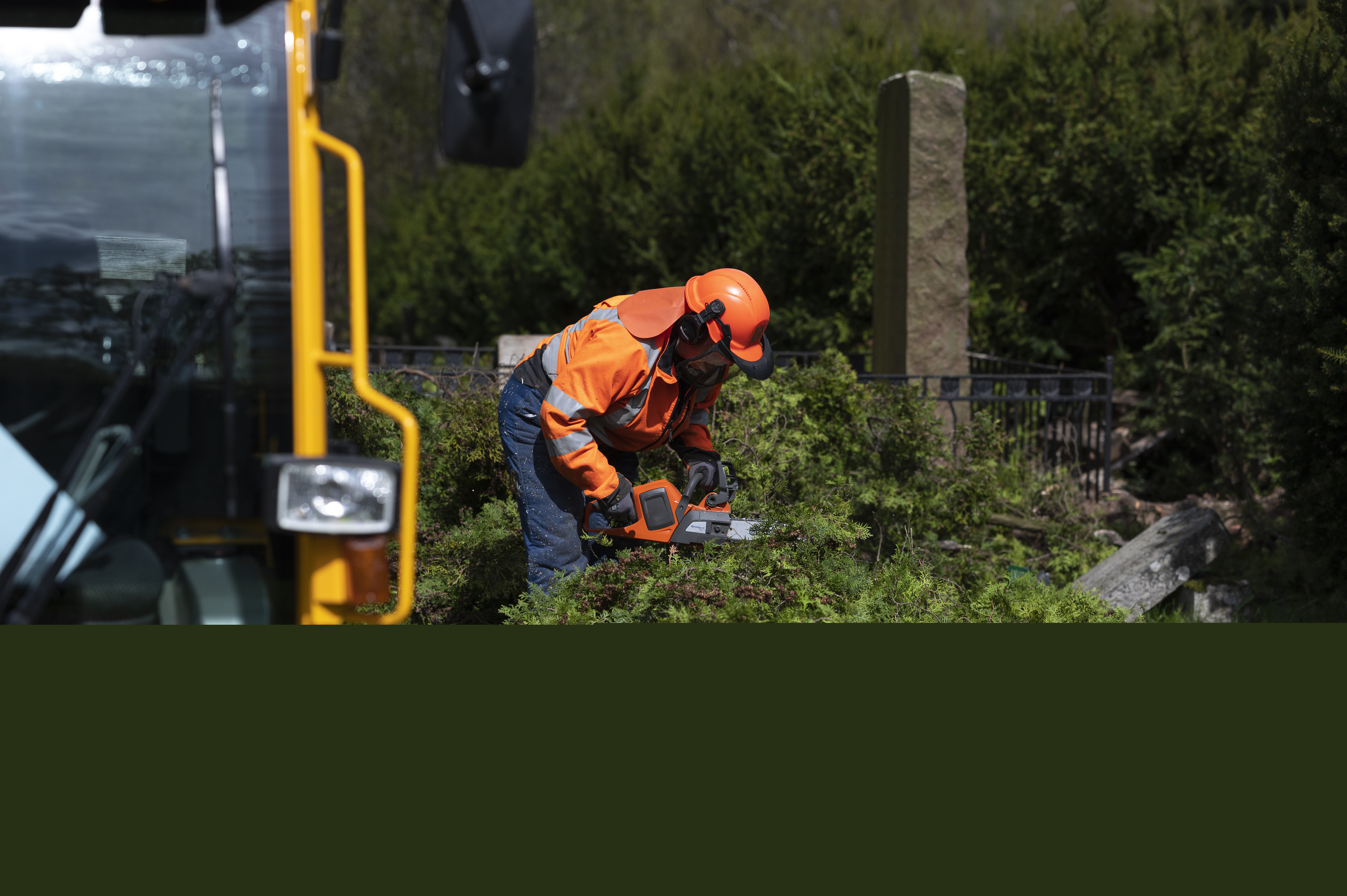 En kyrkogårdsarbetare sågar av ett nedhugget träd med en motorsåg.