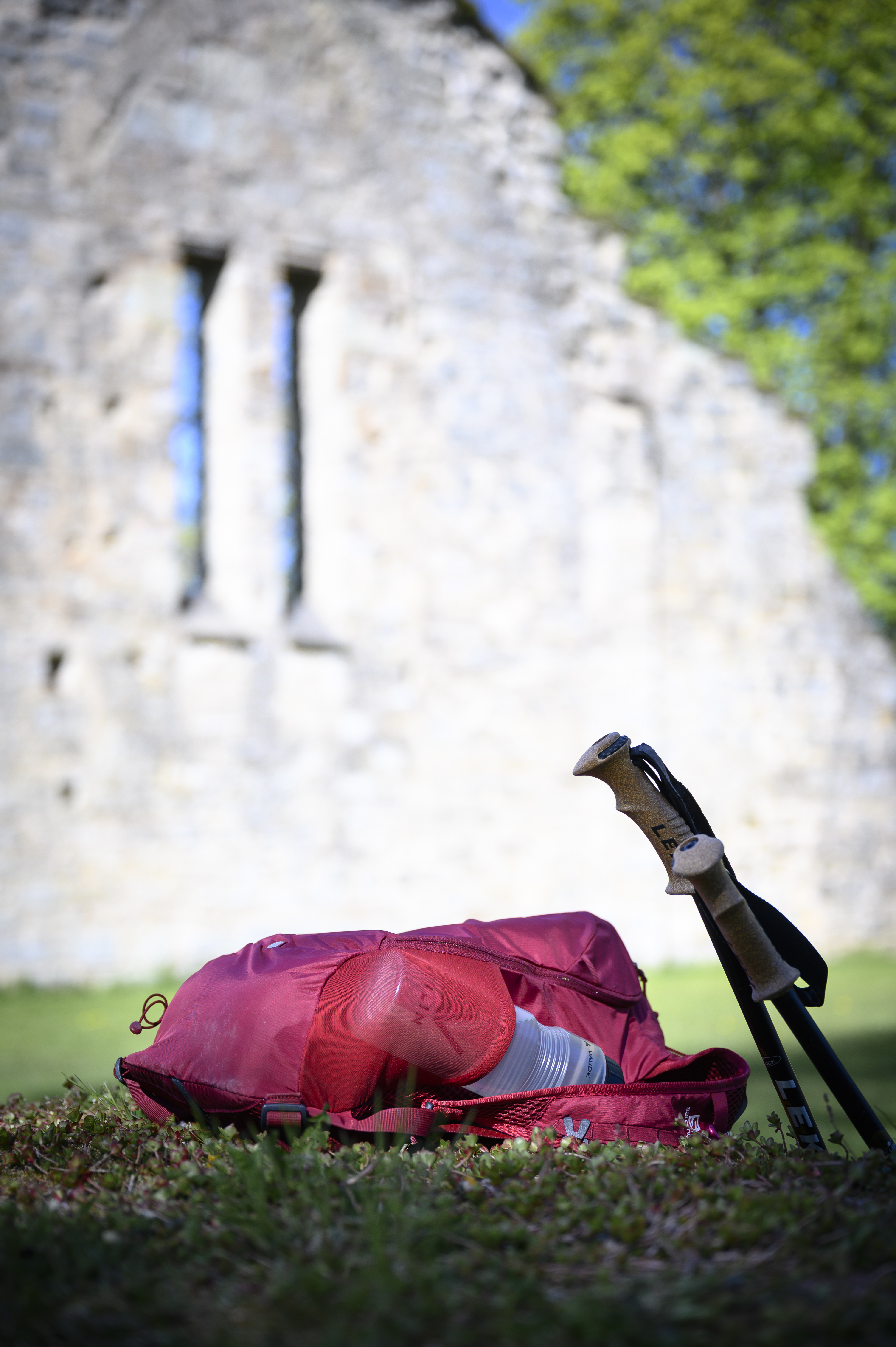 Ett par vandringsstavar och en liten ryggsäck ligger på gräset framför en gammal ruin.