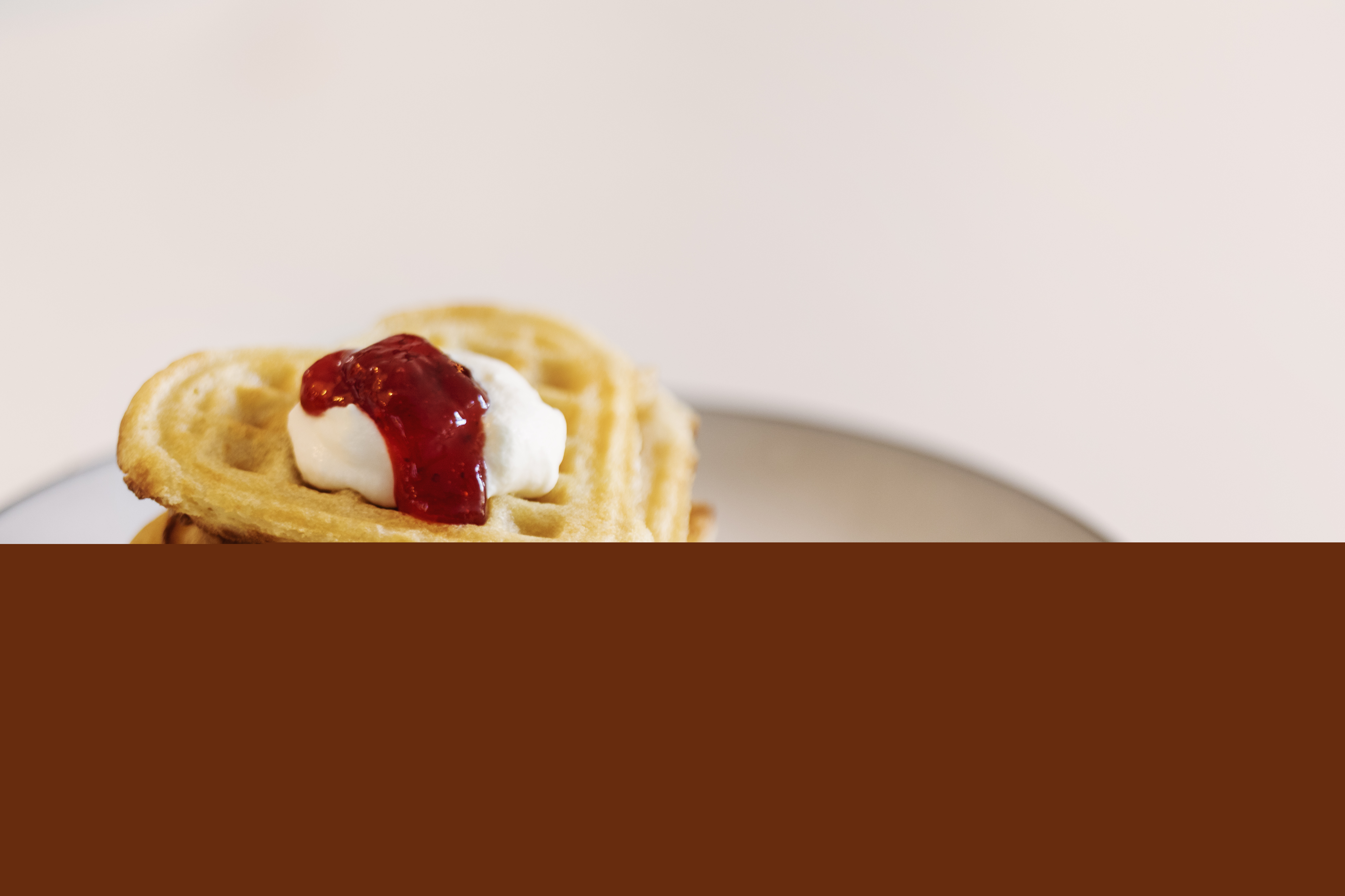 En stapel av hjärtformade våfflor på en tallrik, toppade med grädde och sylt.