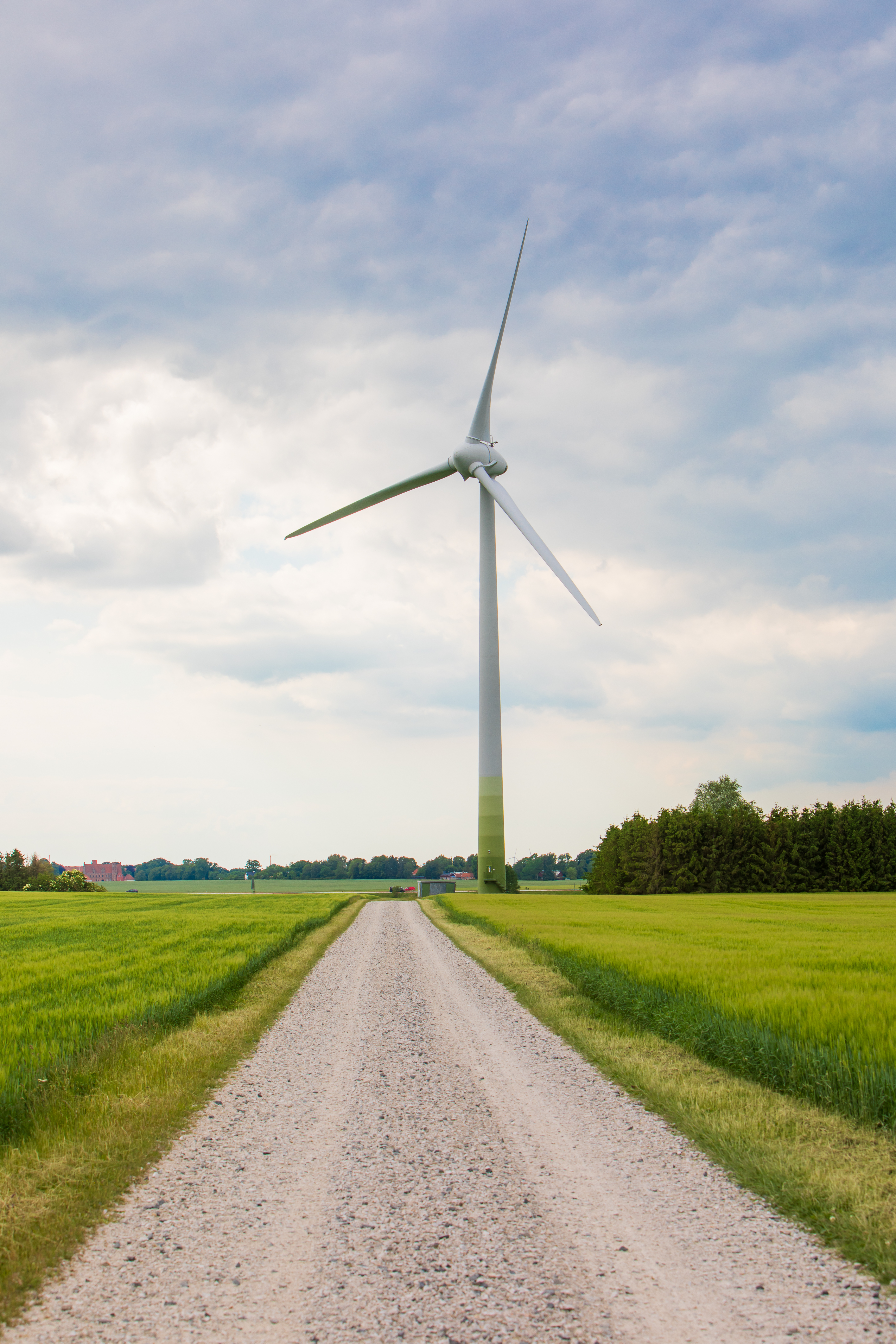 En grusväg leder fram till ett stort vindkraftverk.