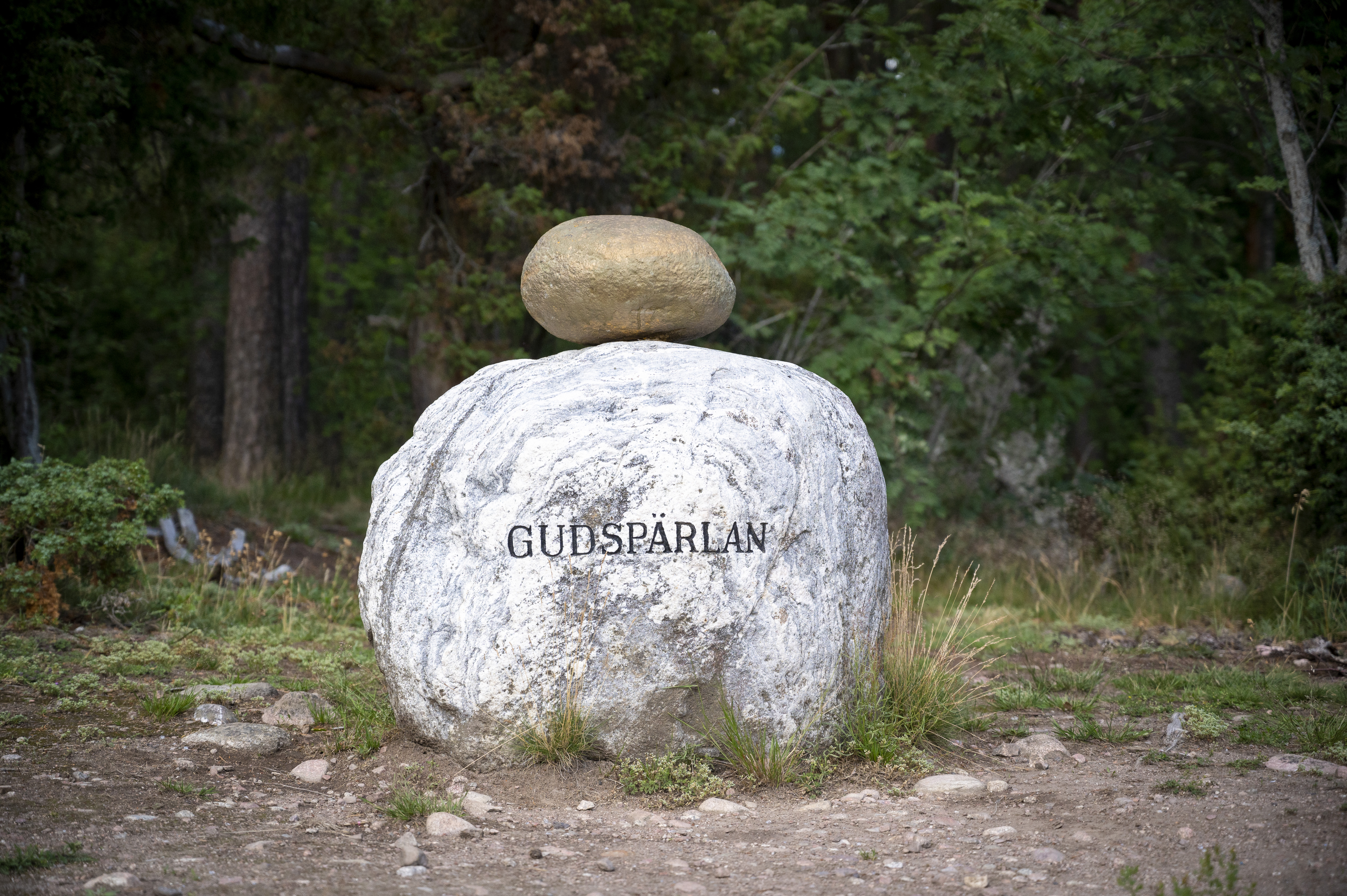 En mindre guldfärgad sten ligger ovanpå en större med texten Gudspärlan.