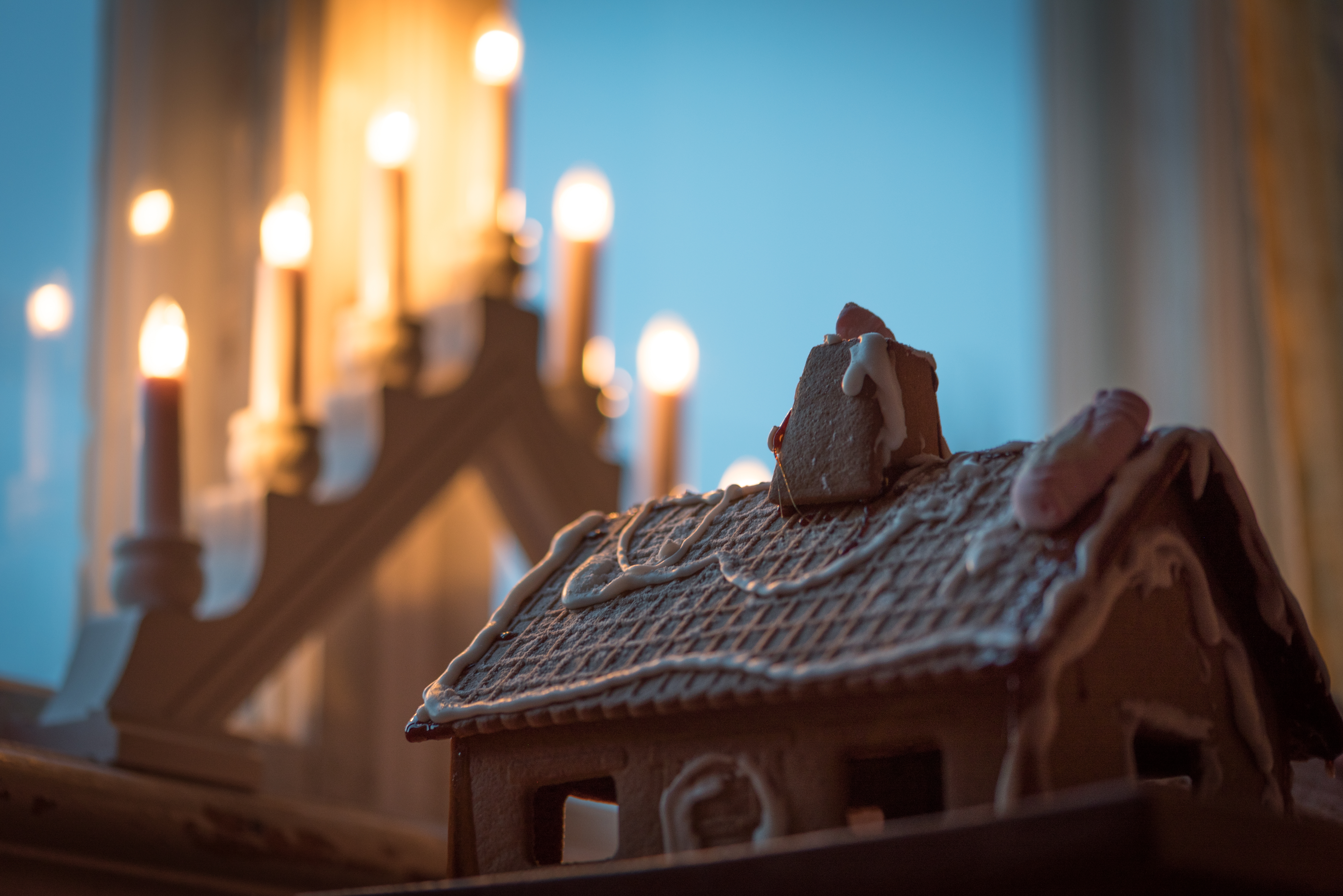 Ett pepparkakshus står framför en adventsljusstake i fönstret.