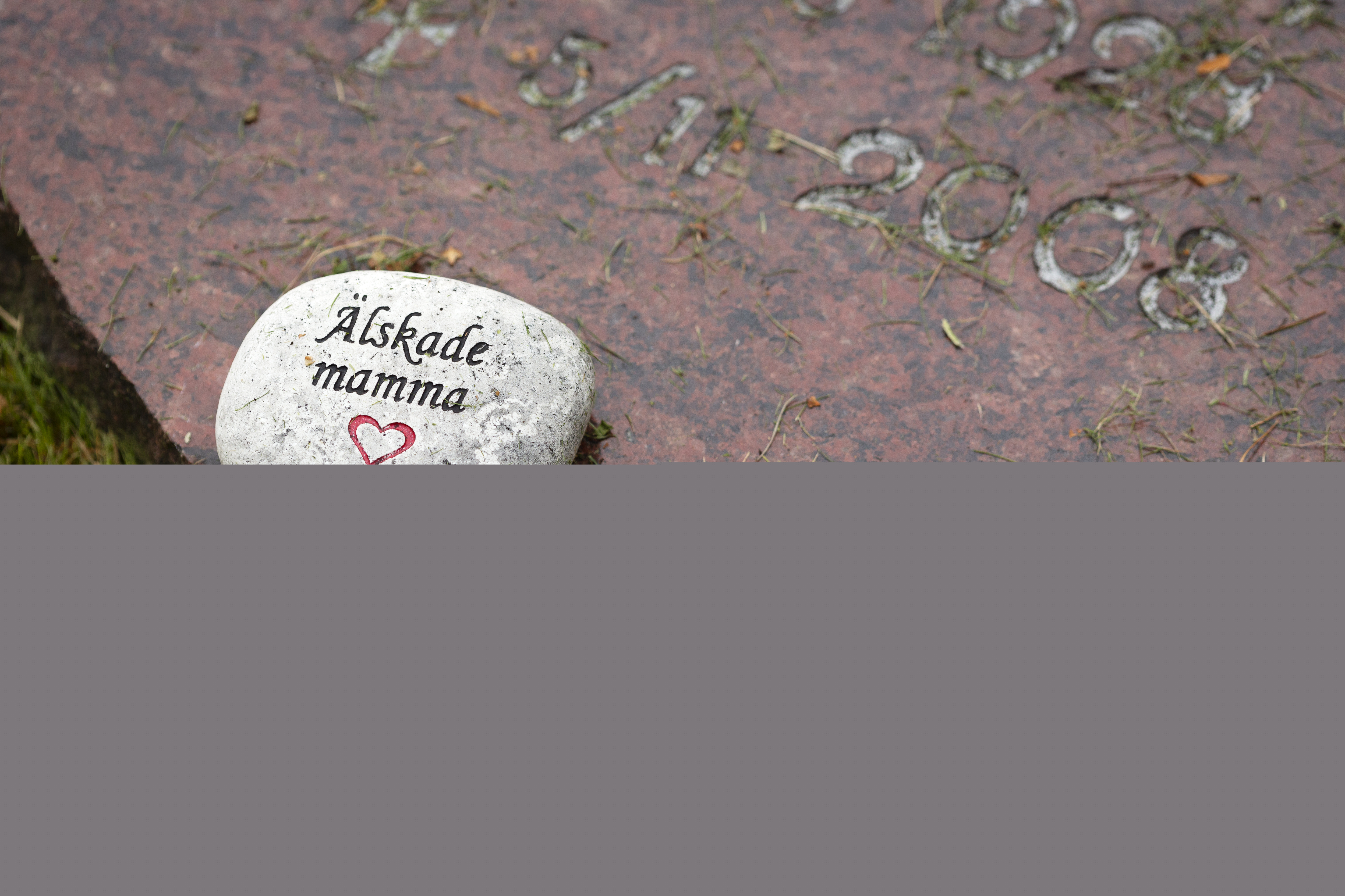 Liten sten med texten "älskade mamma" inristad ligger på en gravsten.