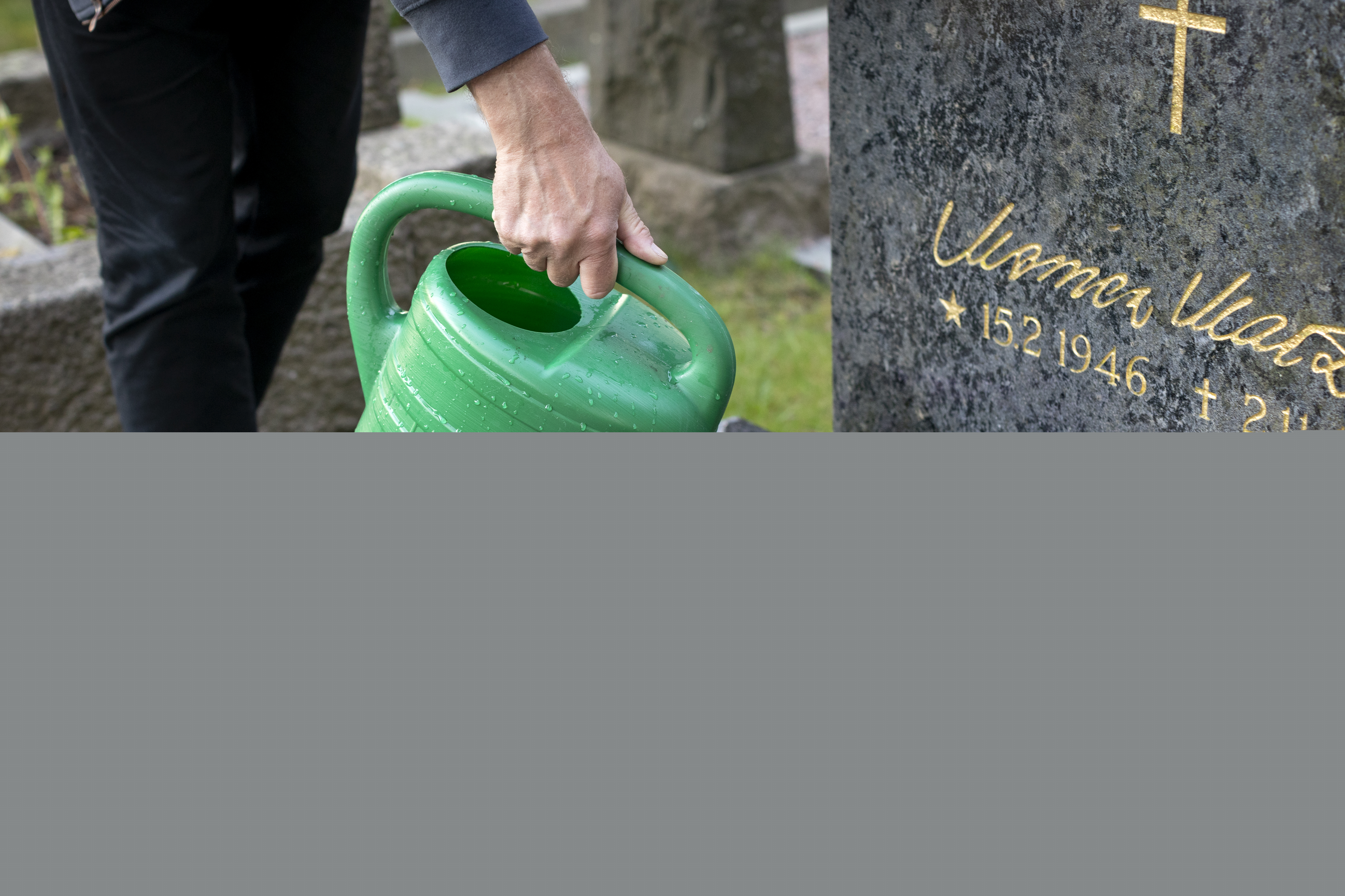 Någon vattnar blommorna på en grav.