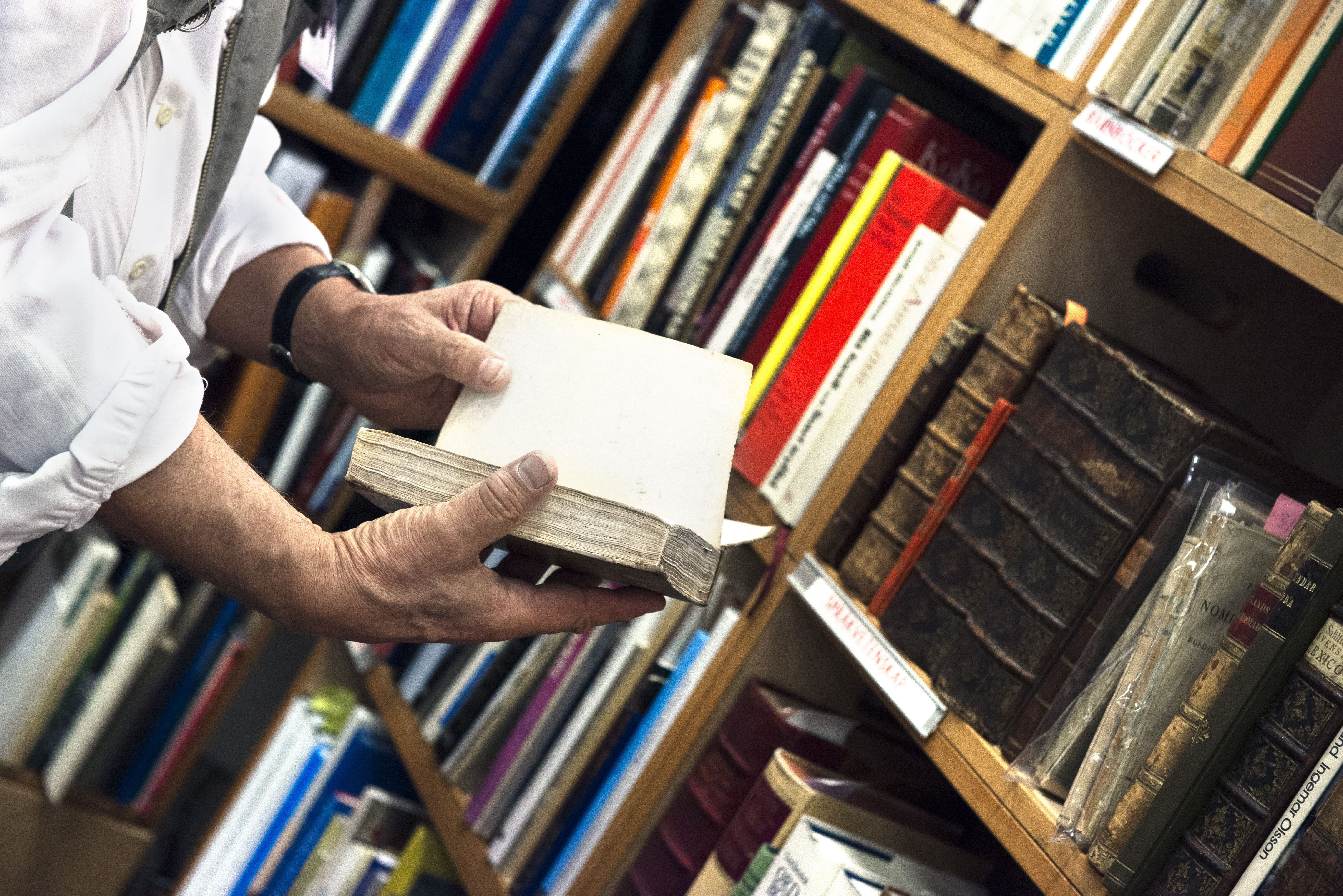 Någon bläddrar i en gammal bok från en bokhylla i ett bibliotek.