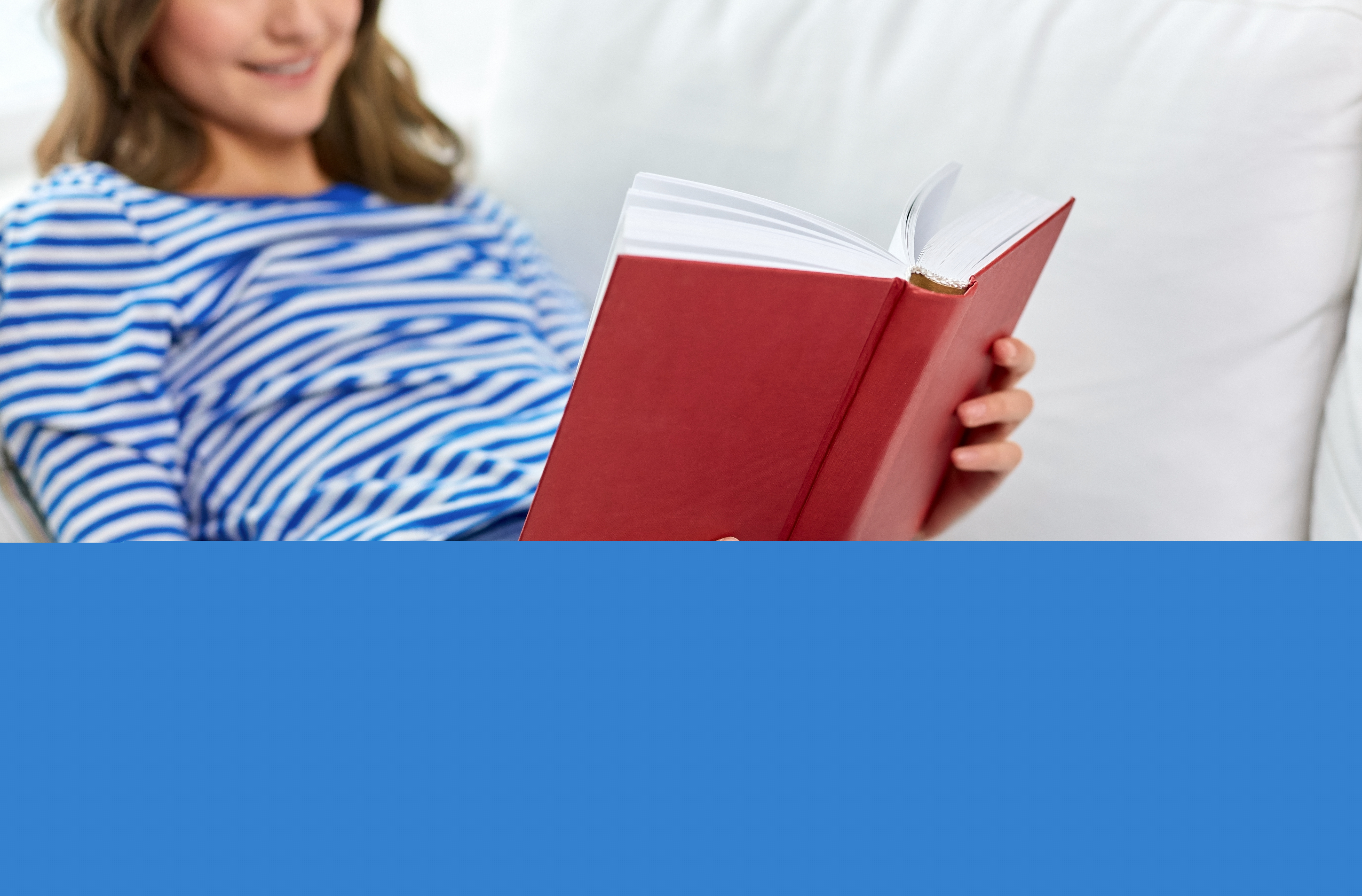 En ung tjej ligger i en soffa och läser ur en röd bok.