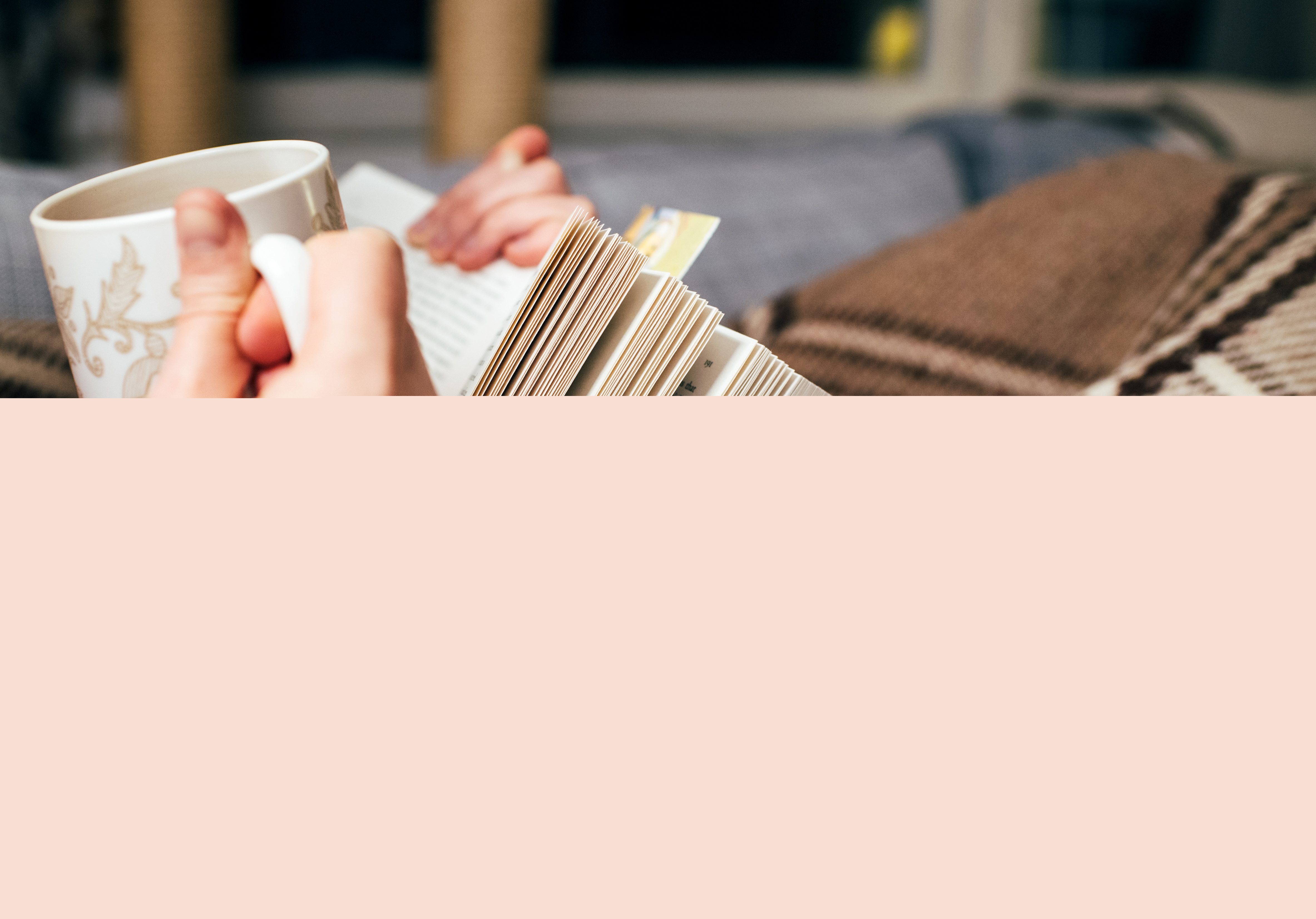 Närbild på någon som ligger under en filt och läser med kopp i handen.