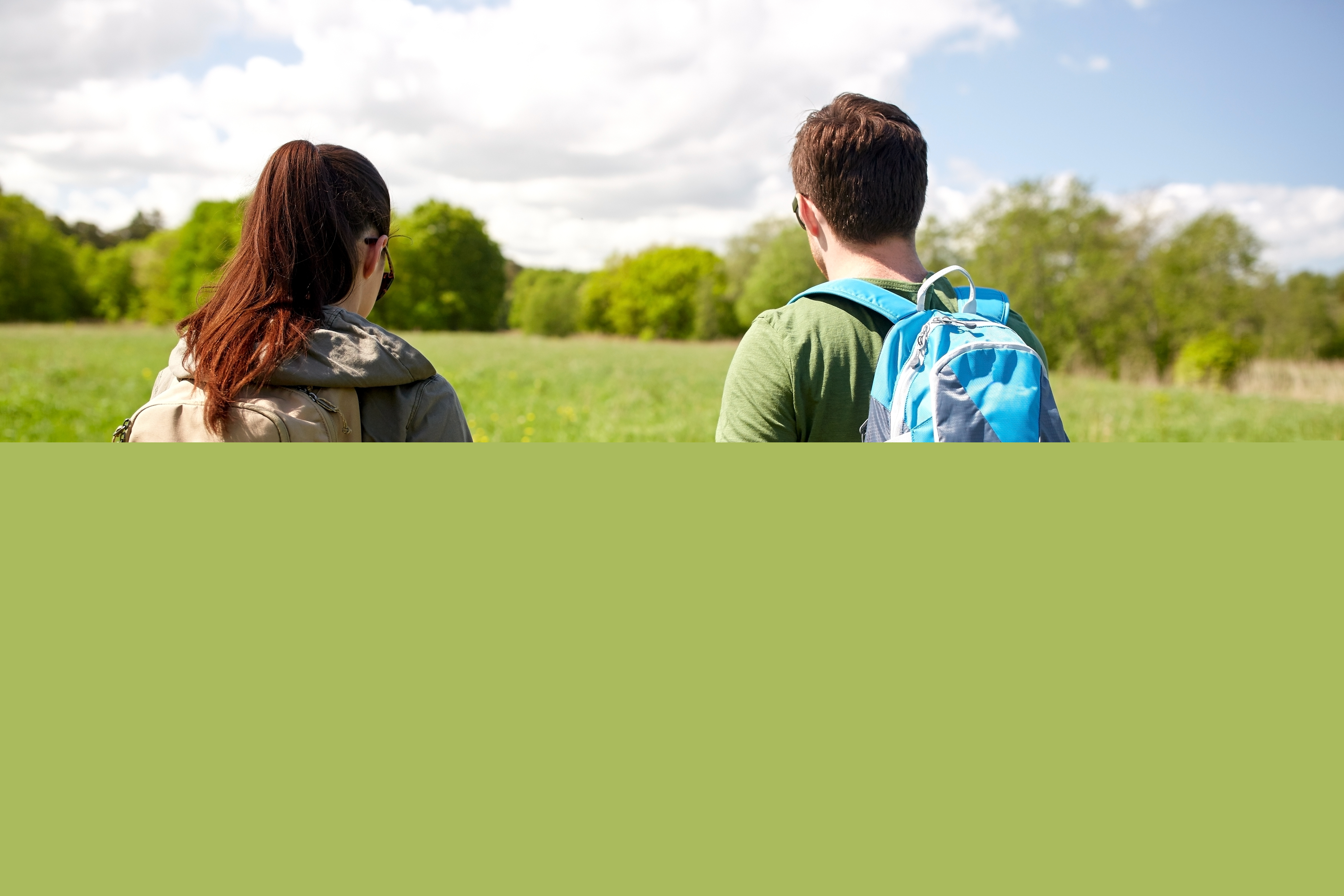 Ett par med packning på ryggen går hand i hand på en äng i solen.