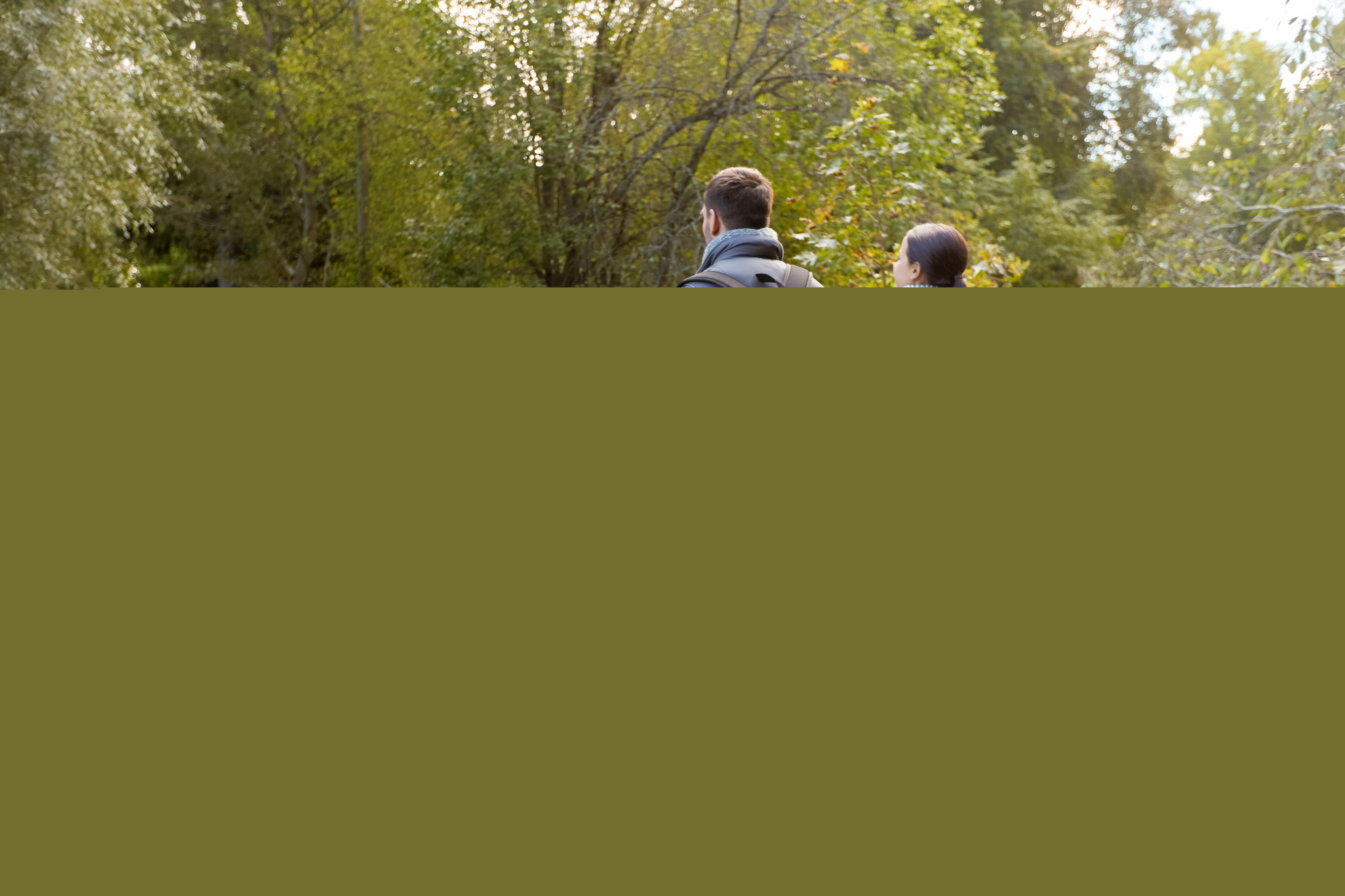 En familj med två barn går hand i hand på en vandringsled i skogen.