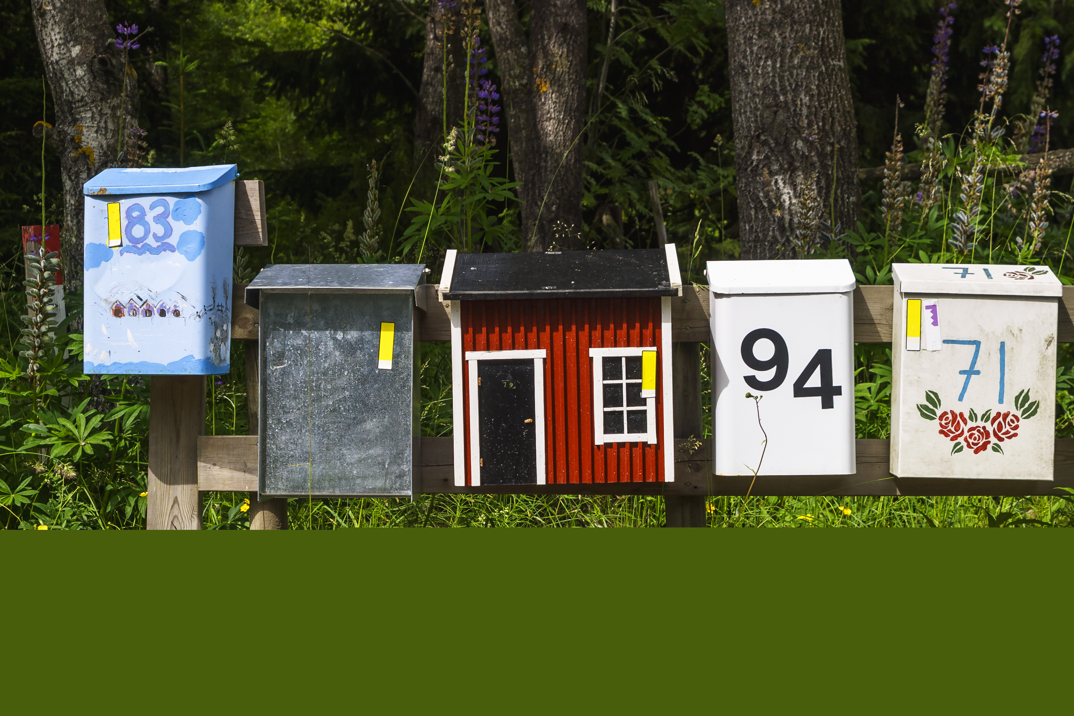 Fem färgglada brevlådor bredvid varandra. Kanske till sommarstugor.
