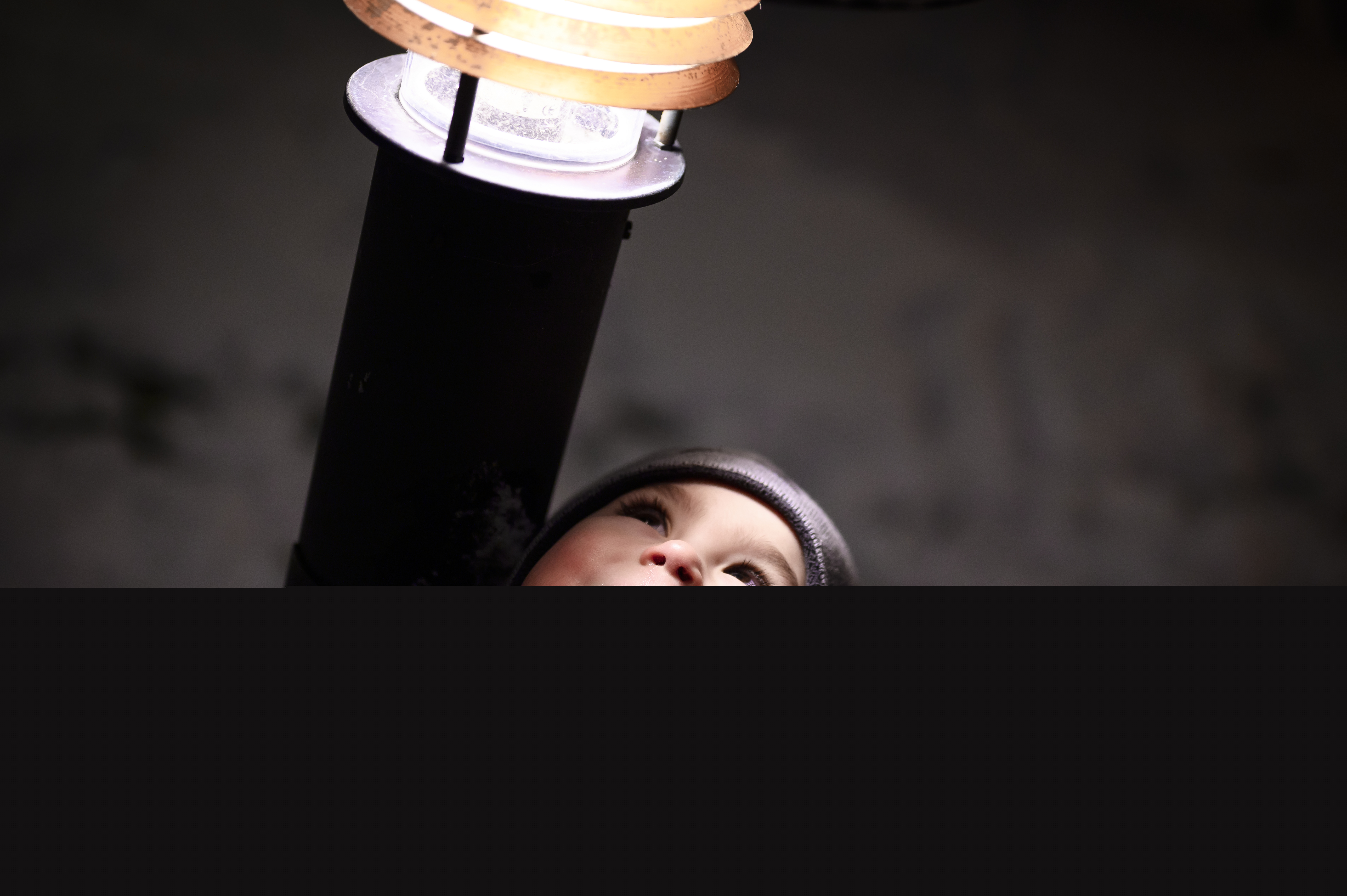 Ett barn står lutat mot en lyktstolpe med ansiktet vänt mot ljuset.