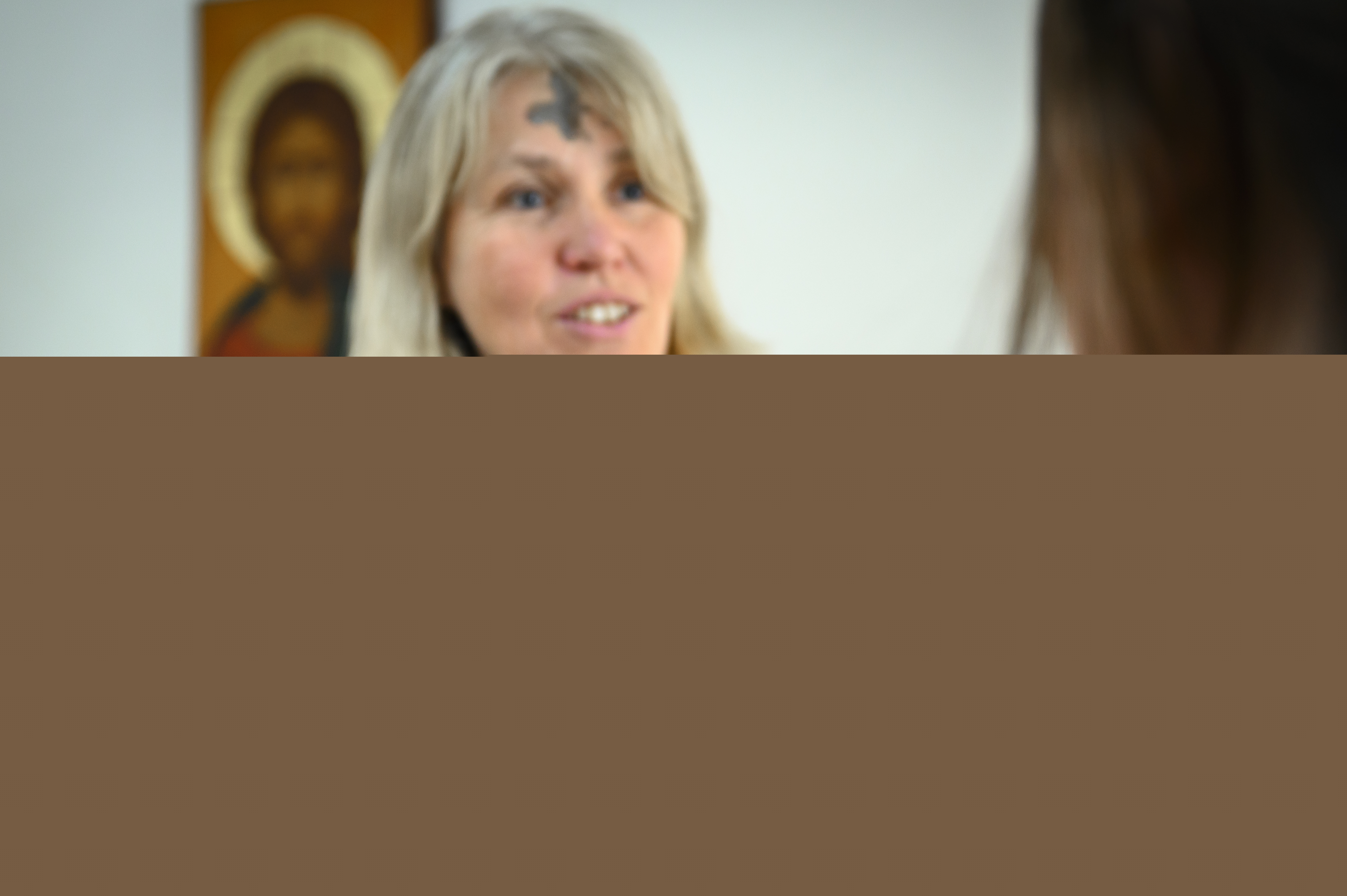 Kvinnlig präst med askkors i pannan har doppat fingret i askan för att göra ett likadant kors på personen framför henne.