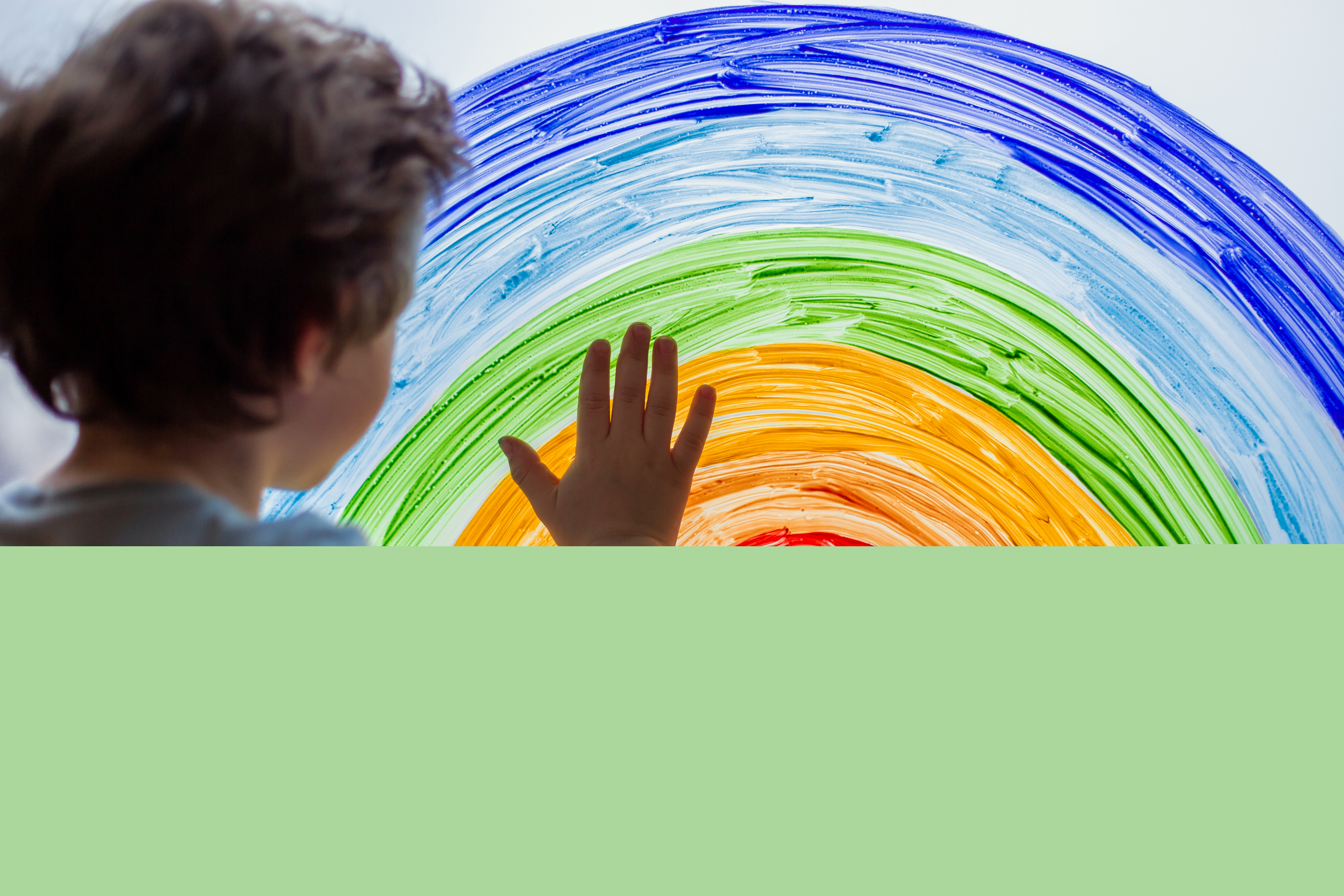 En liten pojke håller handen på en regnbåge målad på ett fönster.