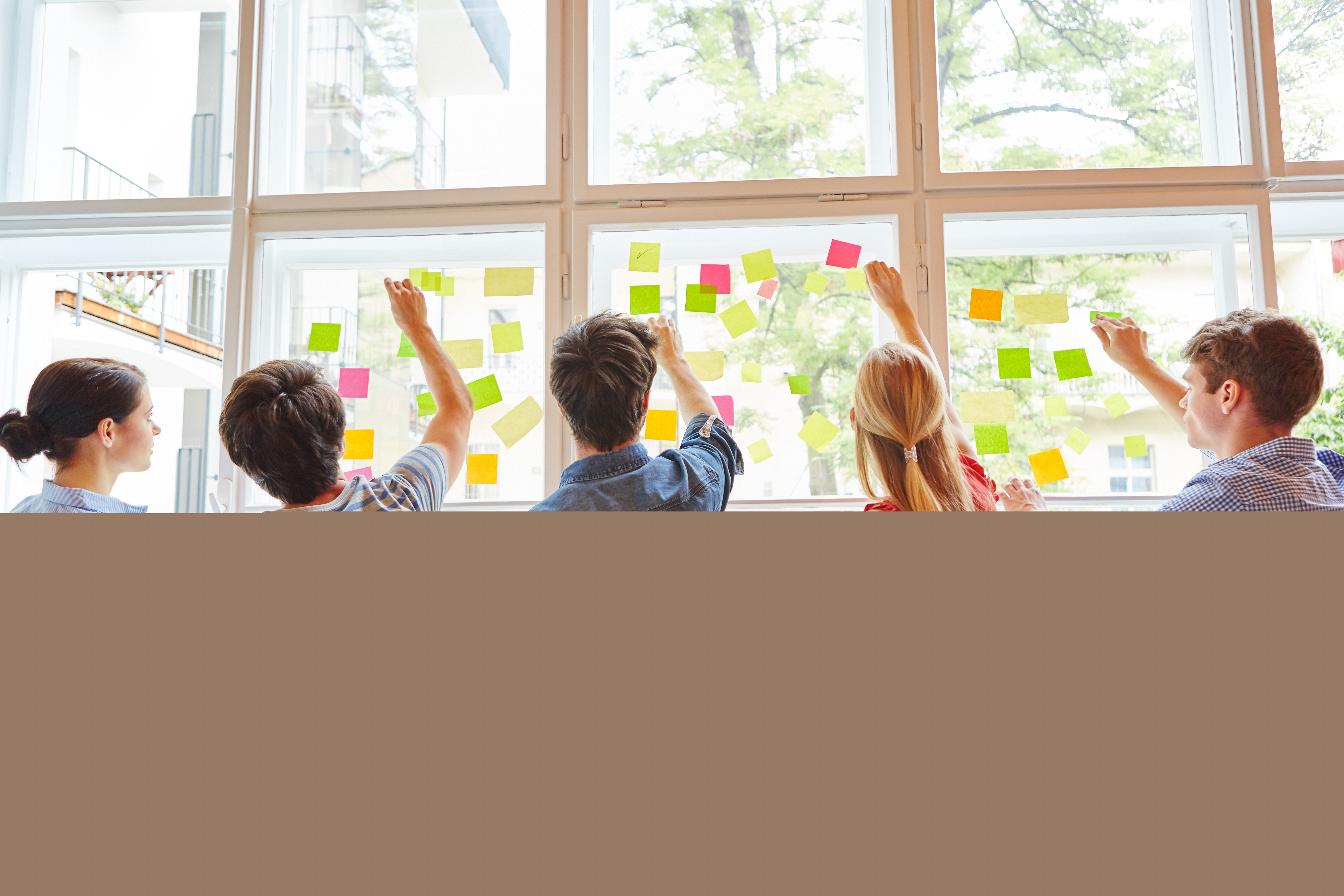 Några ungdomar sätter upp en massa olikfärgade post it-lappar på ett stort fönster.