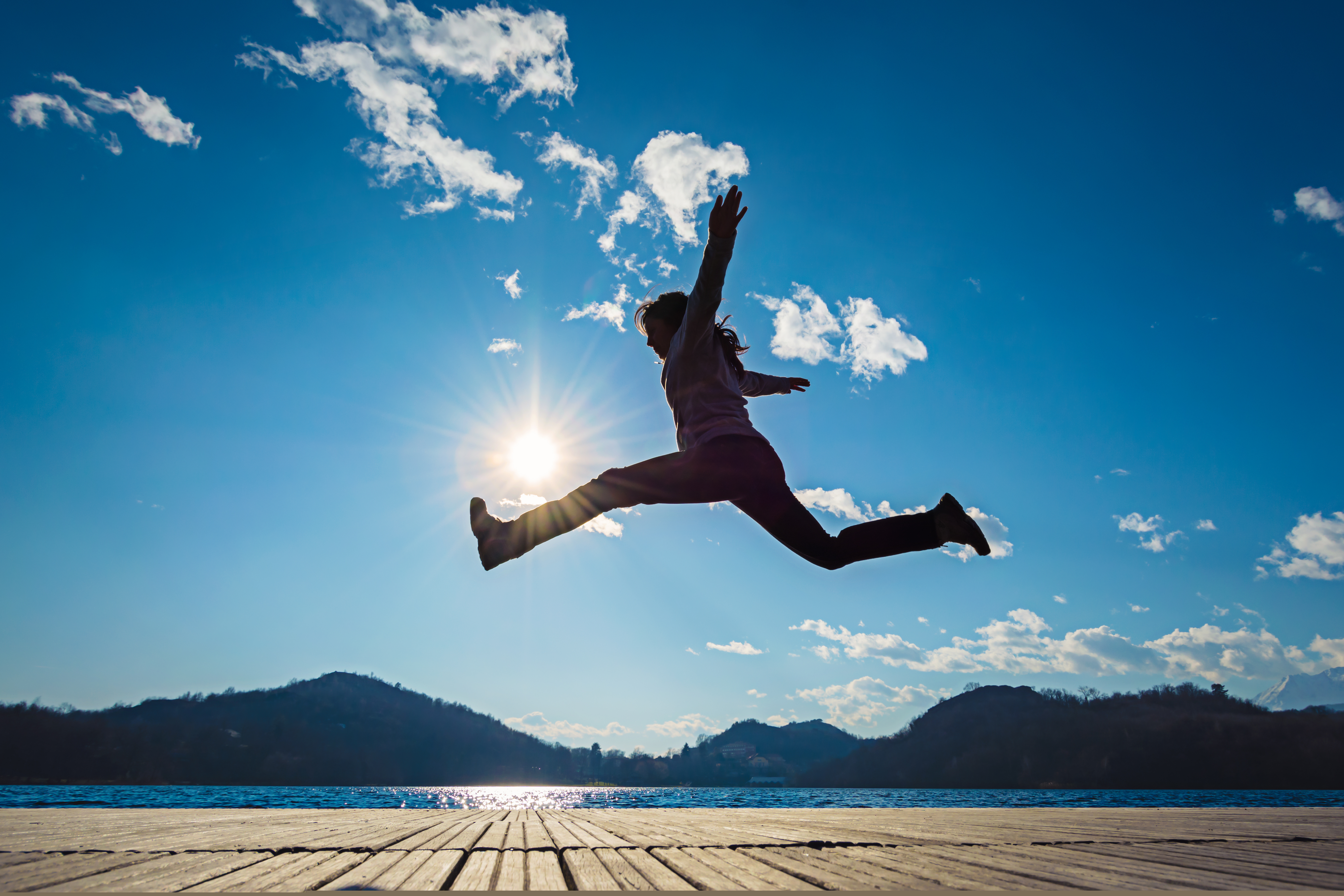 En flicka hoppar på en brygga i solen.