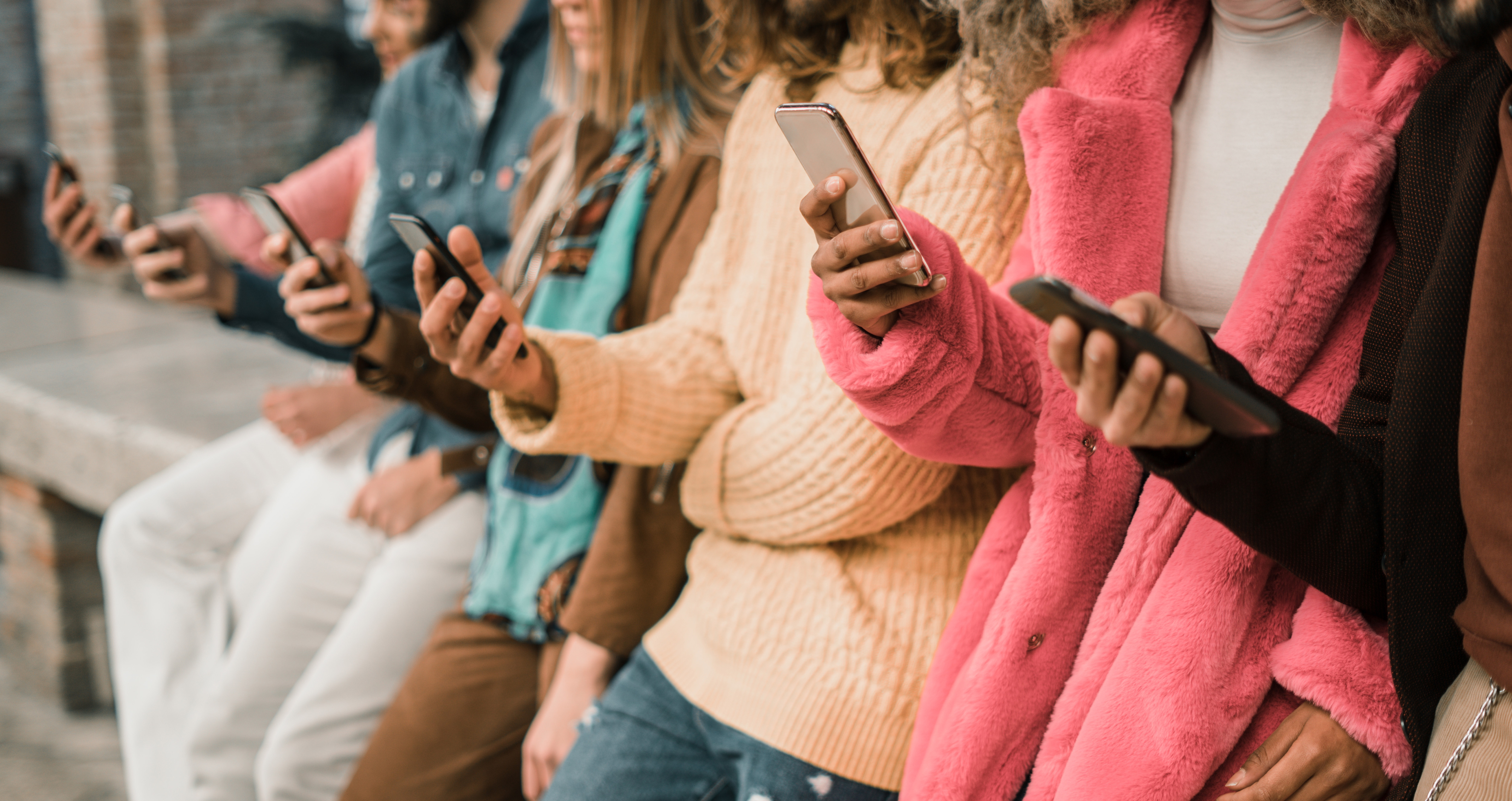 Ett gäng ungdomar står på rad med sina mobiltelefoner i handen.