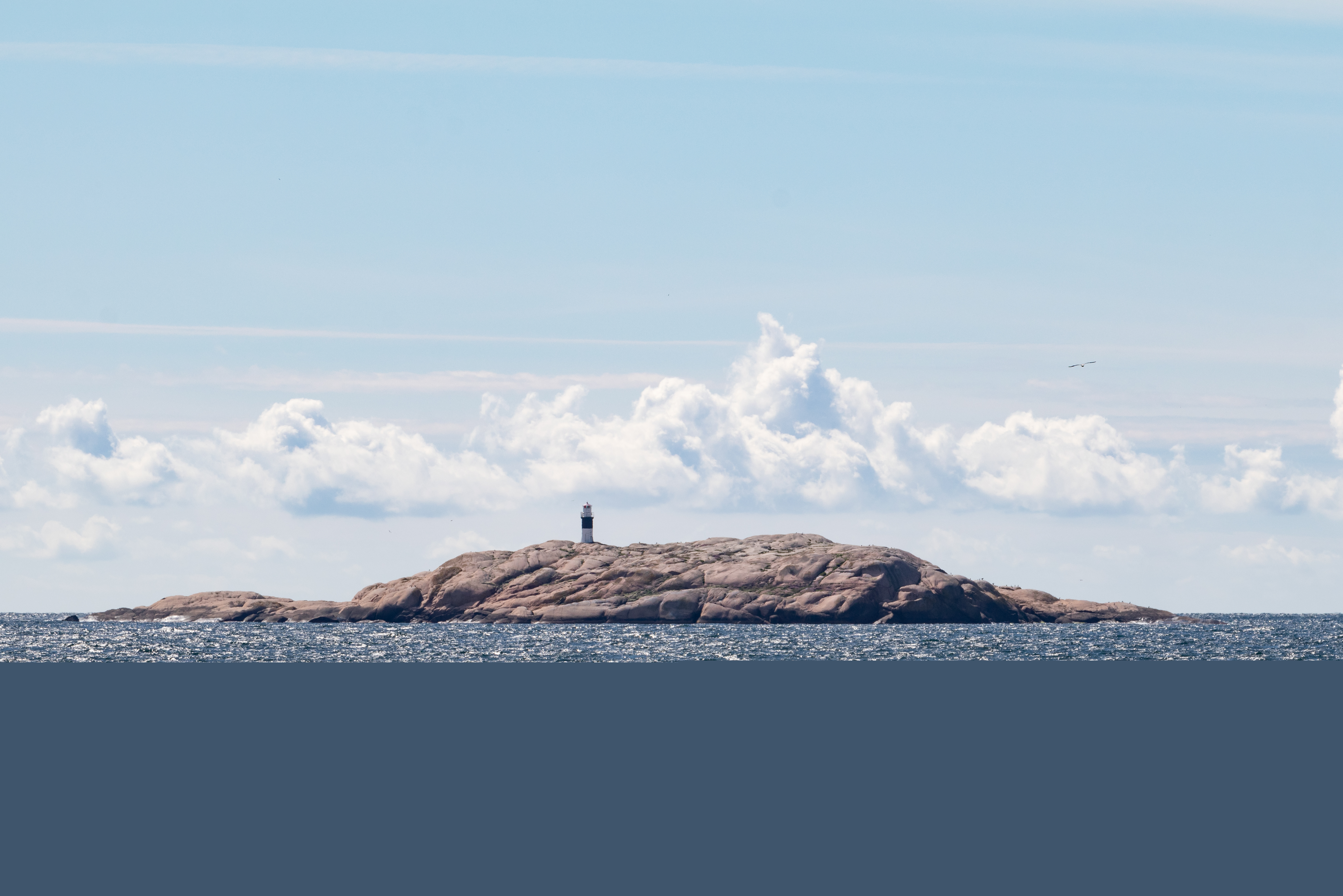 Högst upp på en klippa i havet står en fyr.