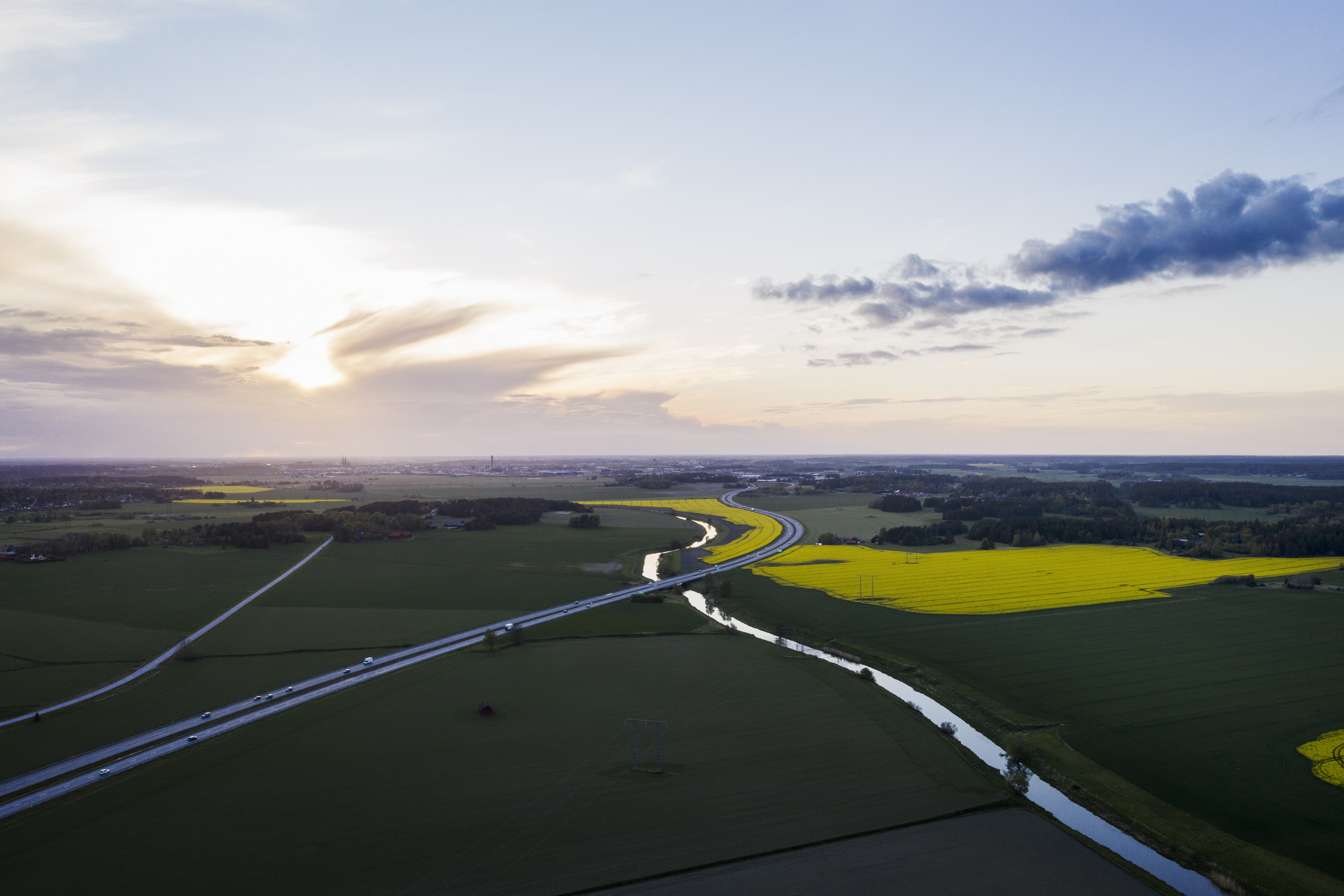 Flygfoto över en bilväg och en å genom ett fält.