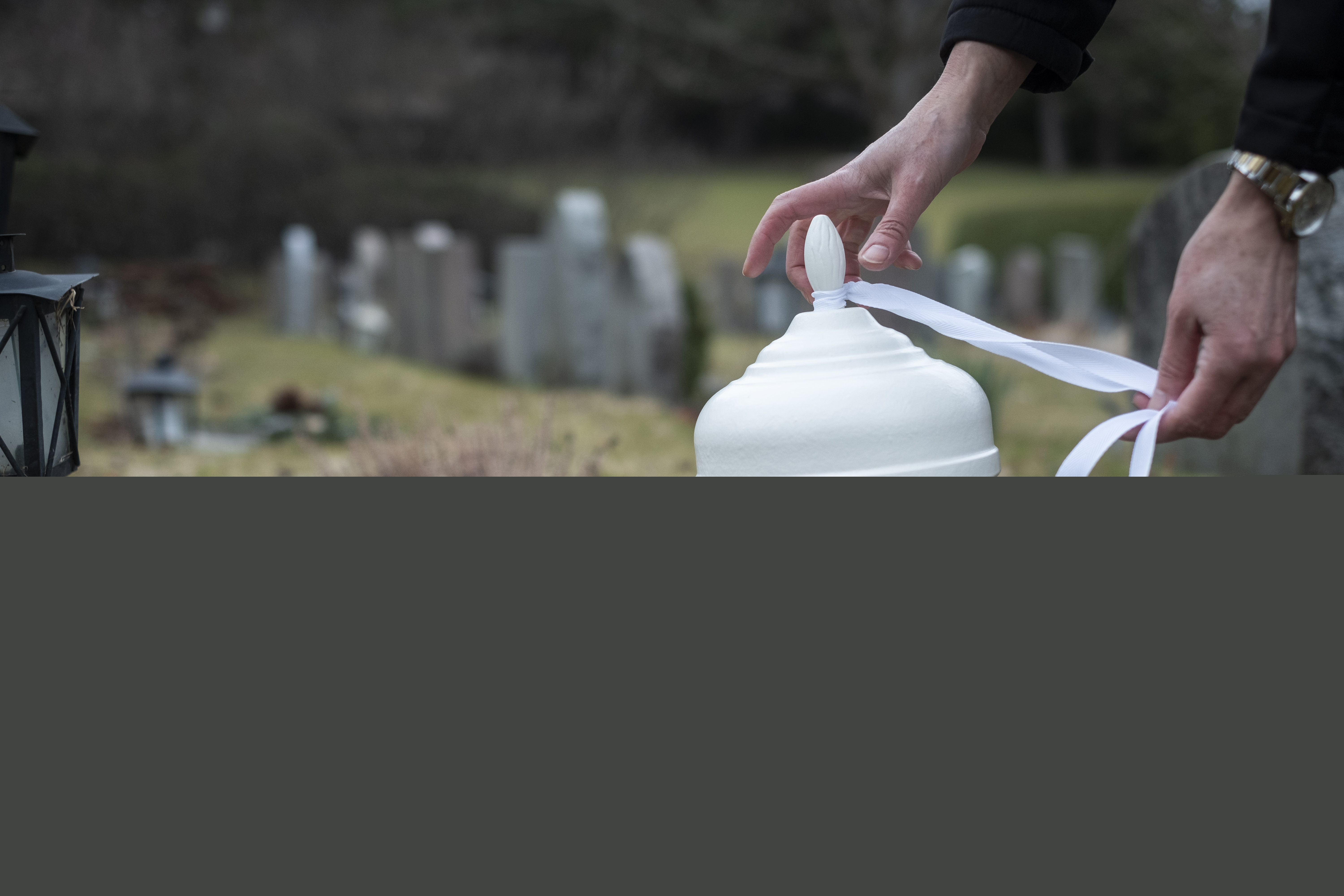 Någon knyter ett vitt band runt en vit urna på en kyrkogård.