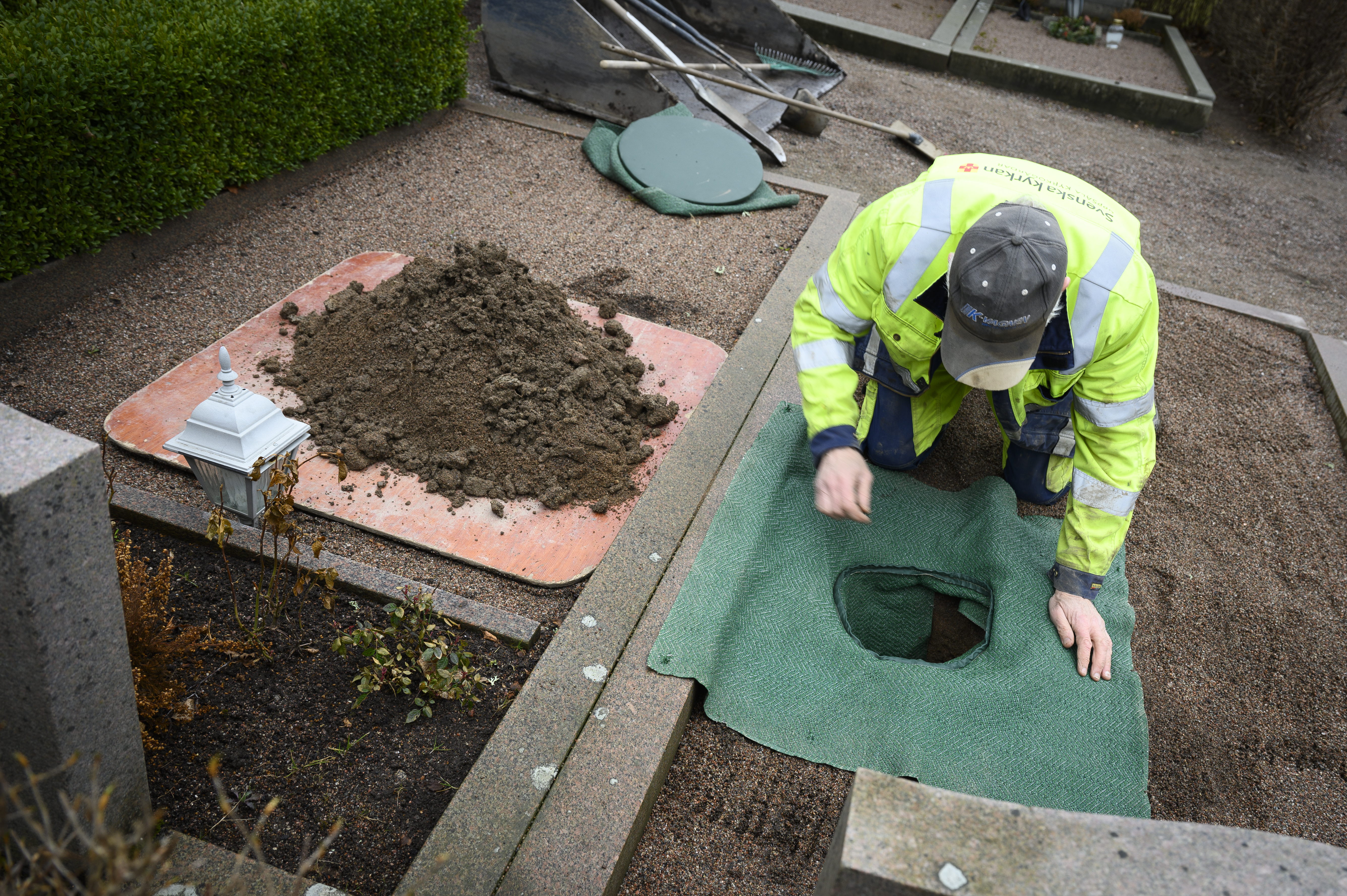 En kyrkogårdsarbetare sitter vid en grav och förbereder en urnsättning.