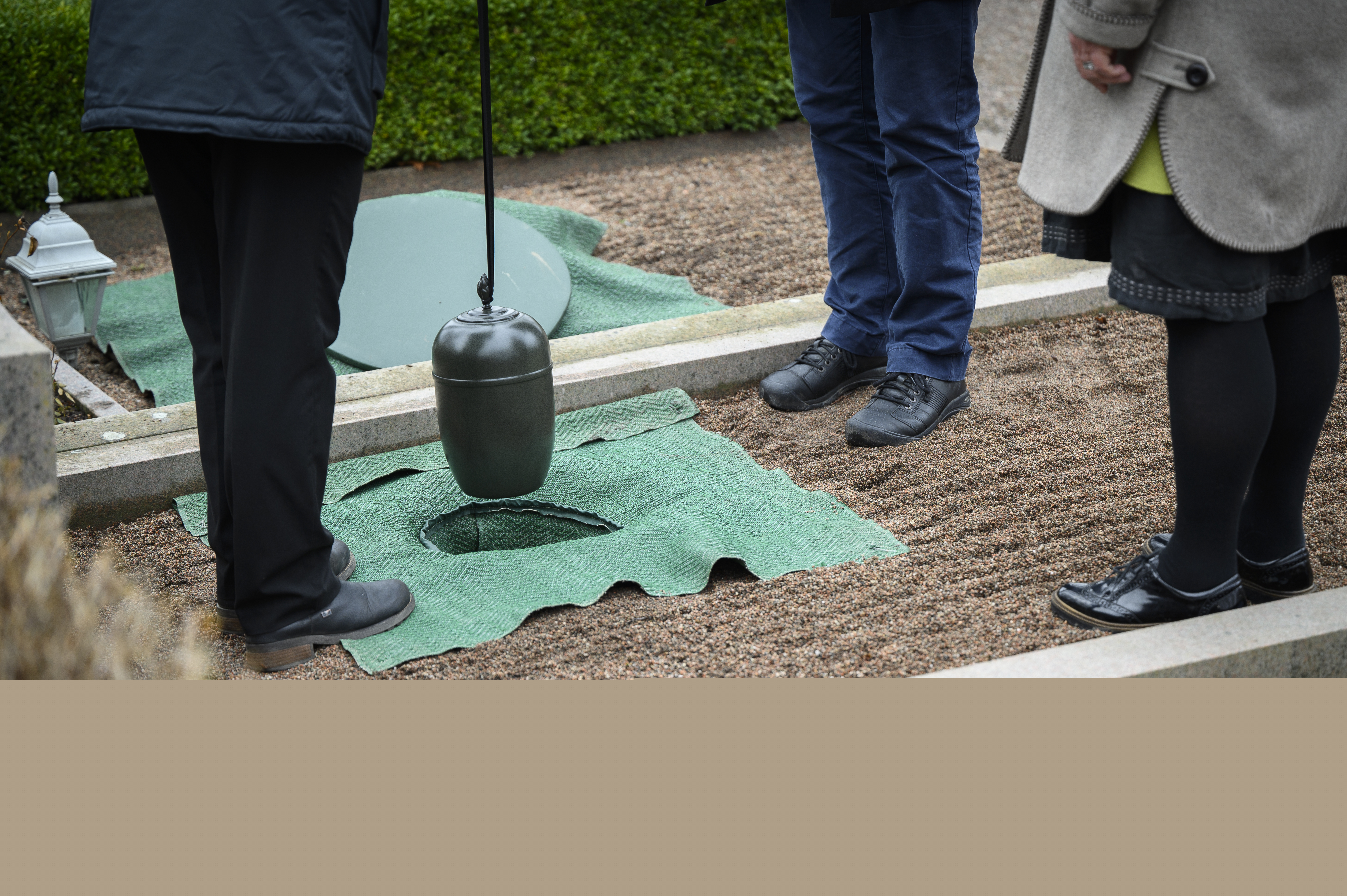 Någon sänker ner en urna i marken på en gravplats.