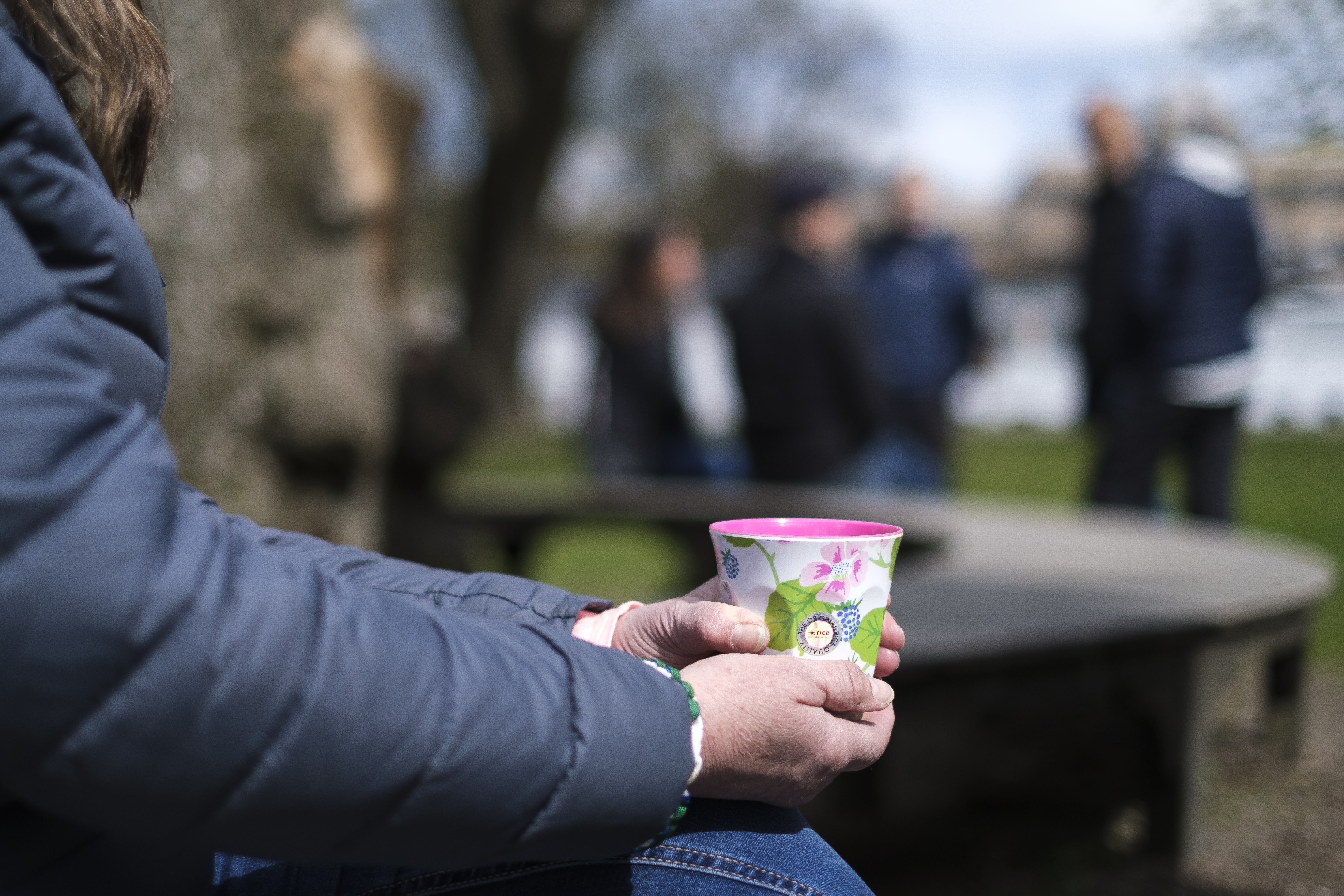 Någon sitter utomhus med en färggrann kopp i händerna.