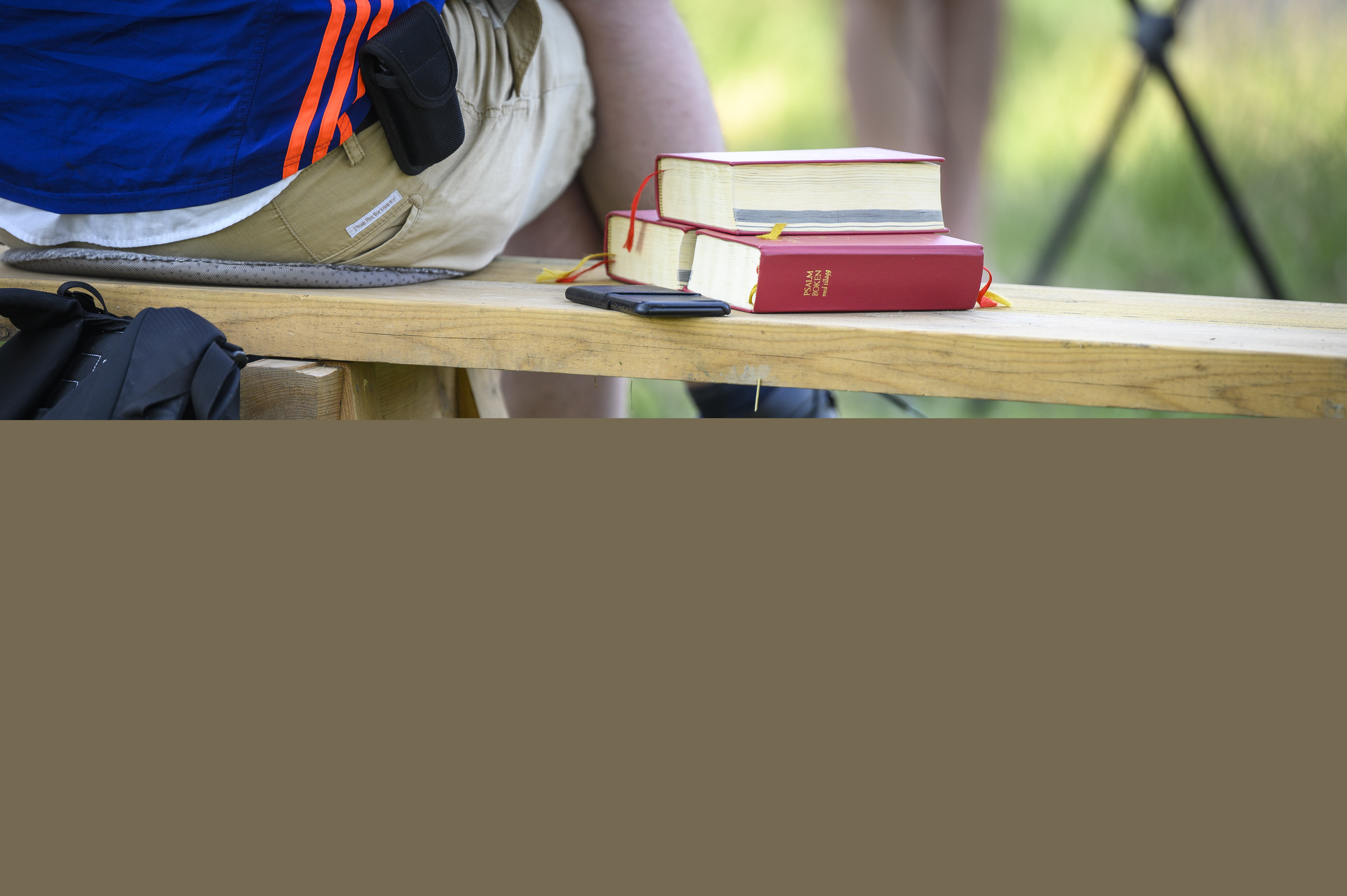Någon sitter på en bänk utomhus. Bredvid ligger några psalmböcker.