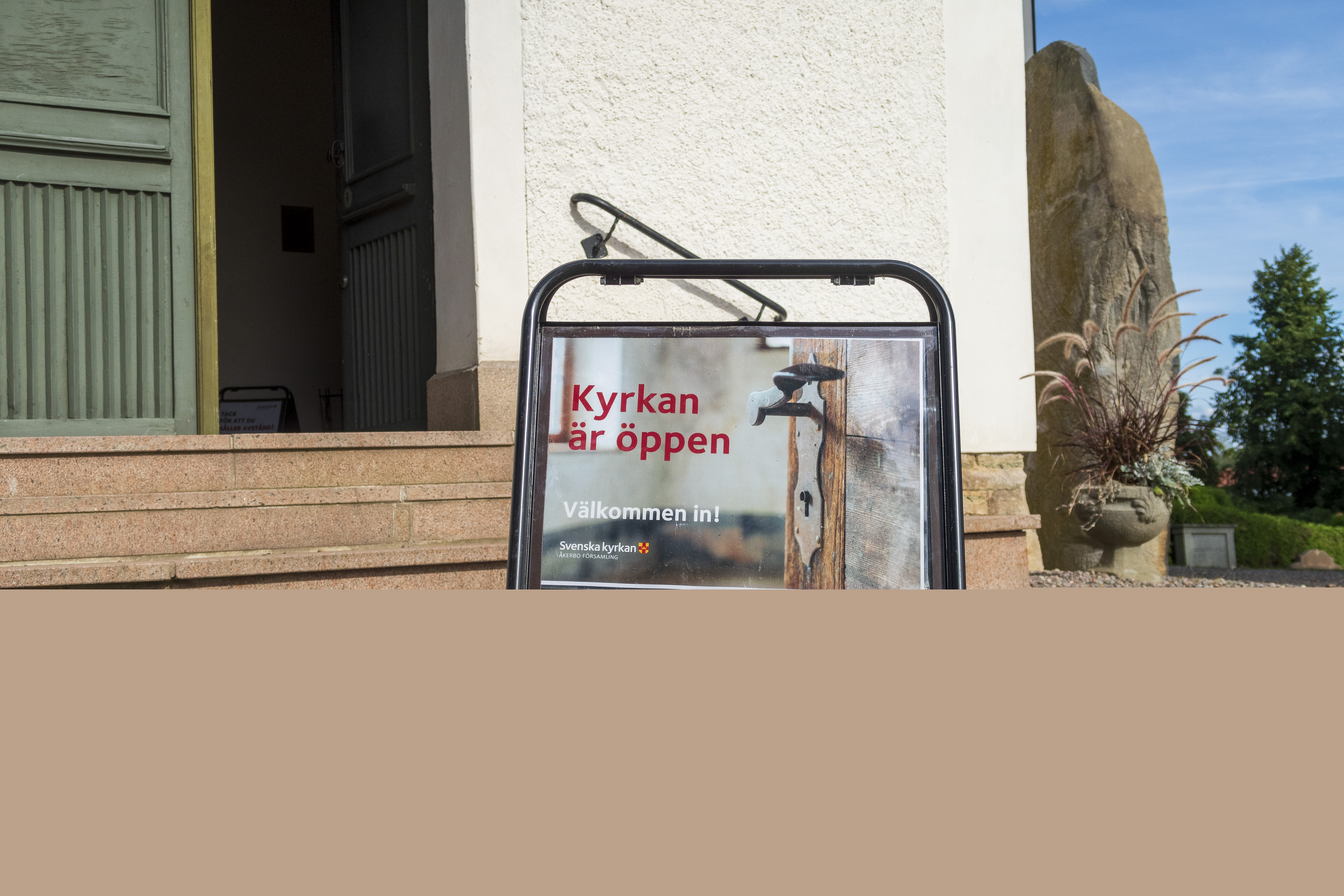 En skylt med texten Kyrkan är öppen står utanför en öppen dörr.