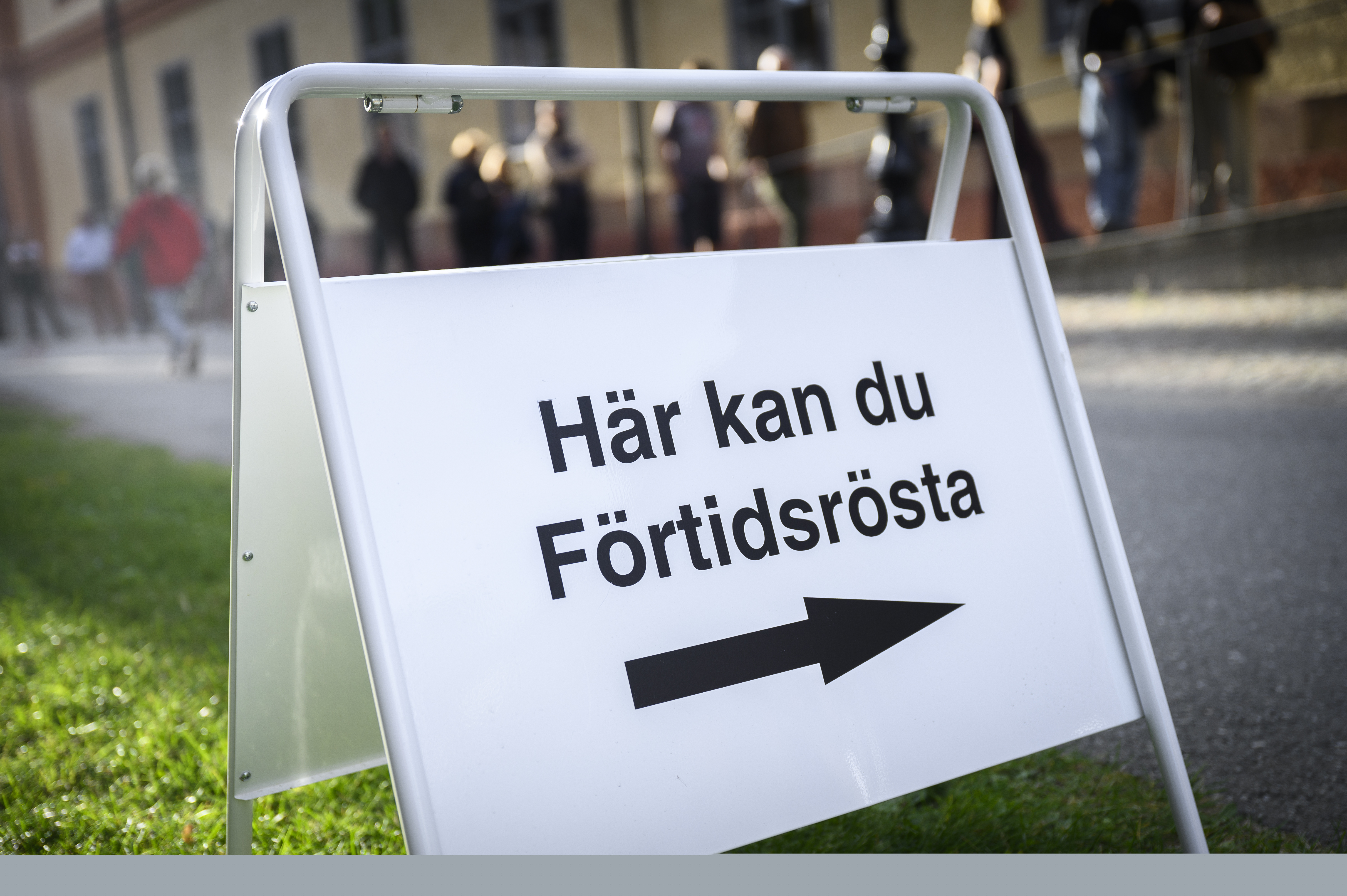 En skylt med texten Här kan du Förtidsrösta. Köande människor i bakgrunden.