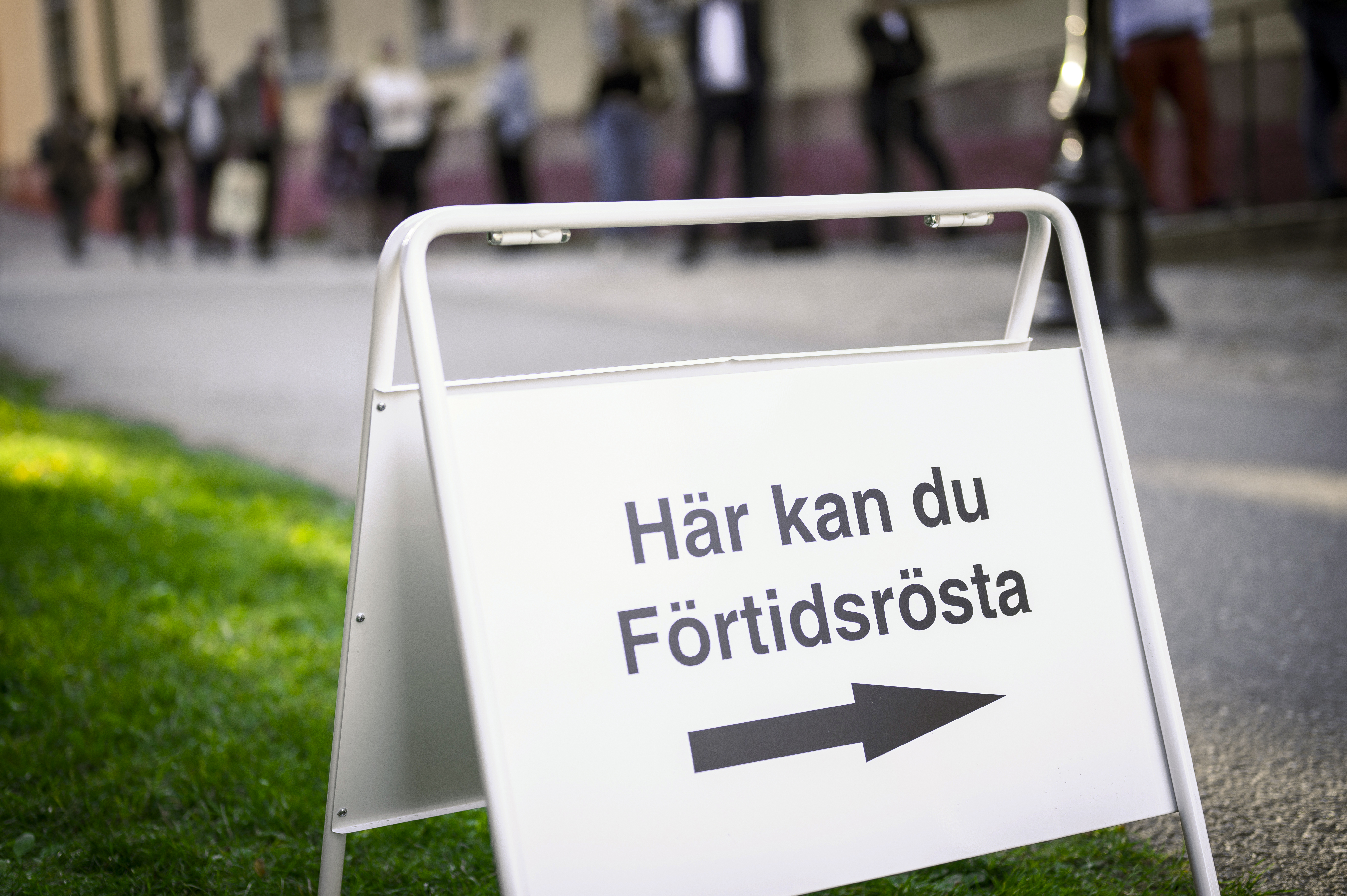 En skylt med texten Här kan du Förtidsrösta. Köande människor i bakgrunden.