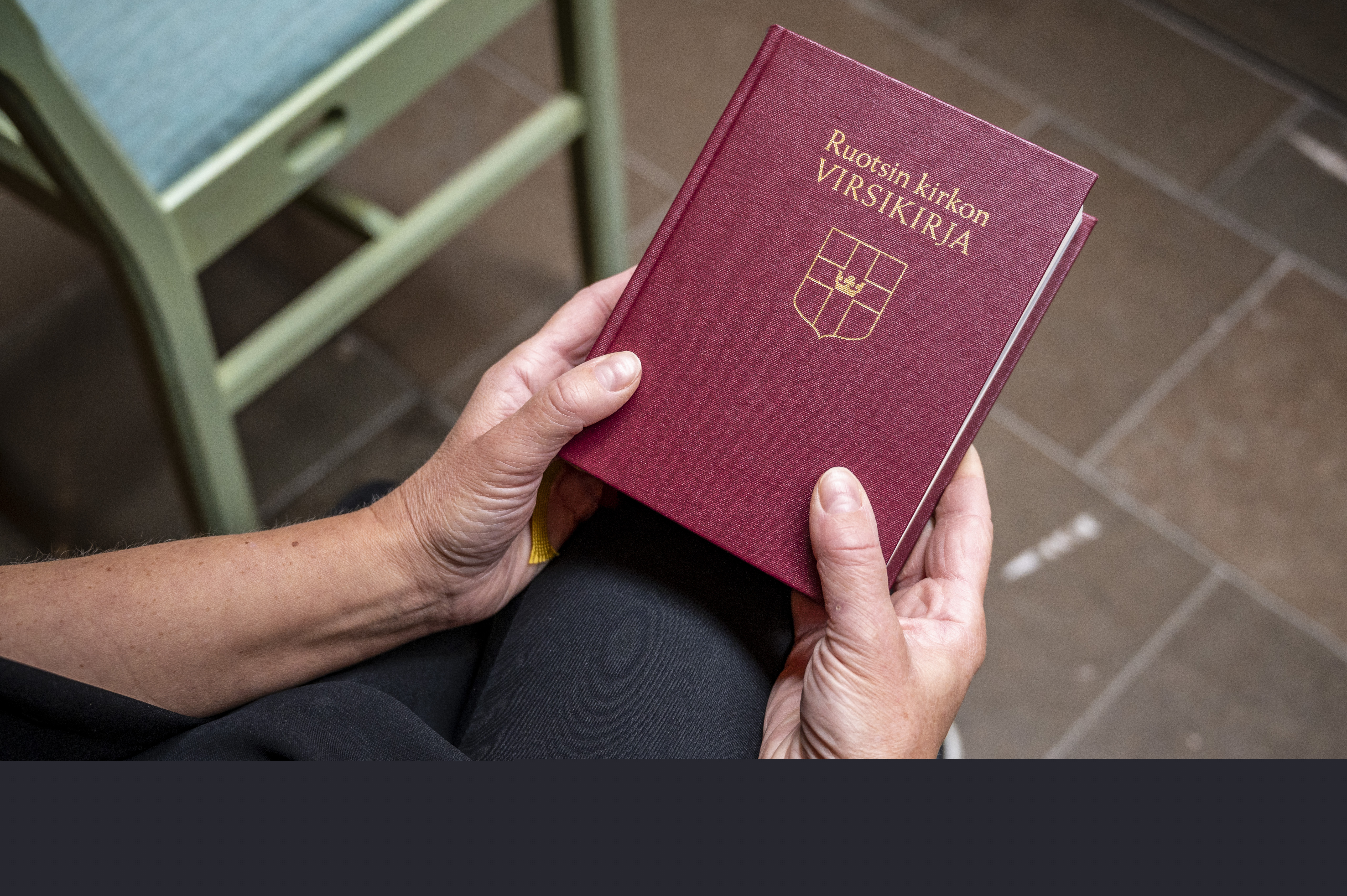 Någon sitter i ett kapell och håller en finsk psalmbok i händerna.