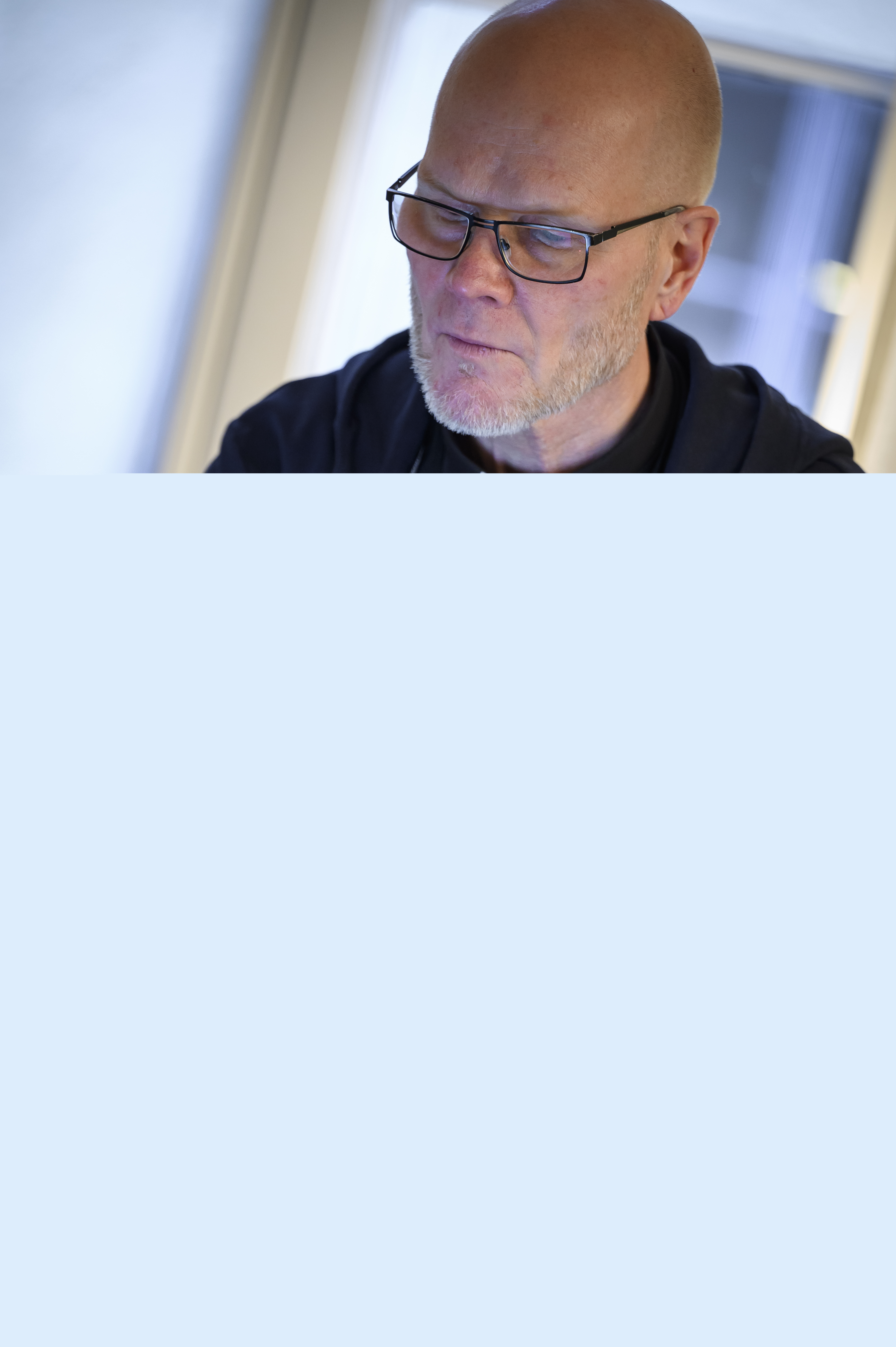 En manlig präst sitter och arbetar på en laptop vid ett bord.