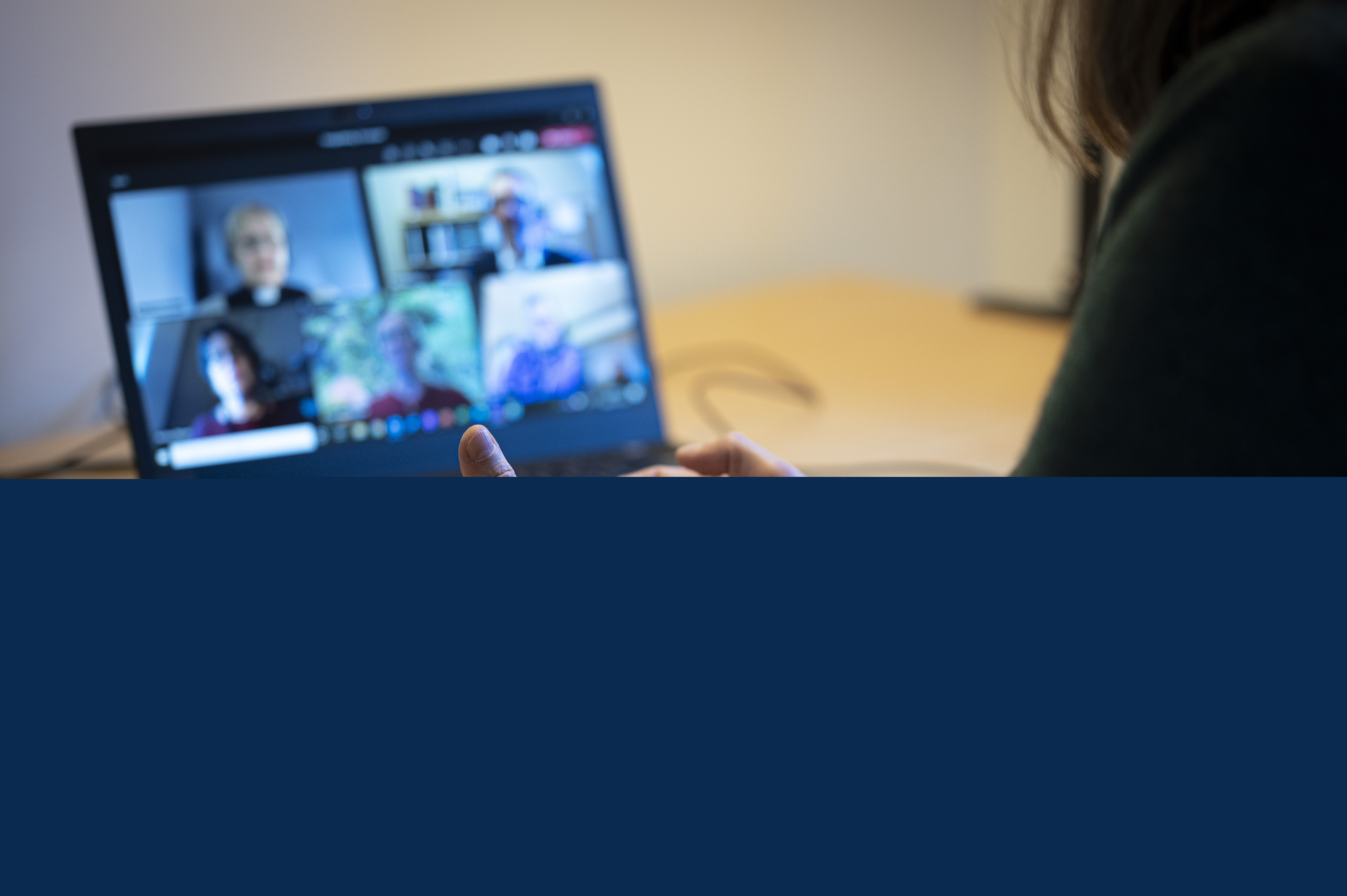 En person sitter vid ett skrivbord och har ett digitalt möte i datorn med några andra.