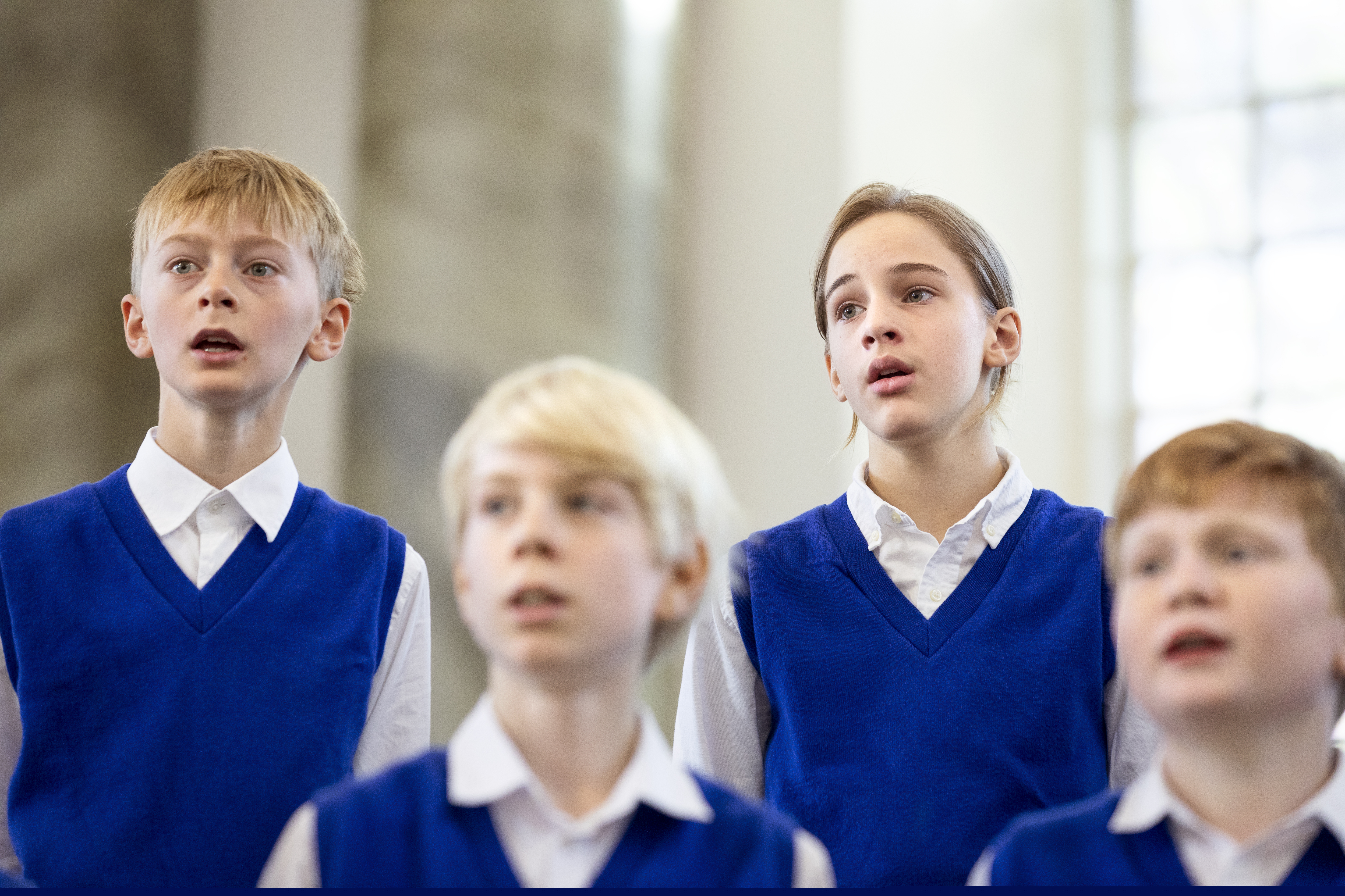 Några medlemmar i en barnkör står och sjunger i blåa slipovrar.