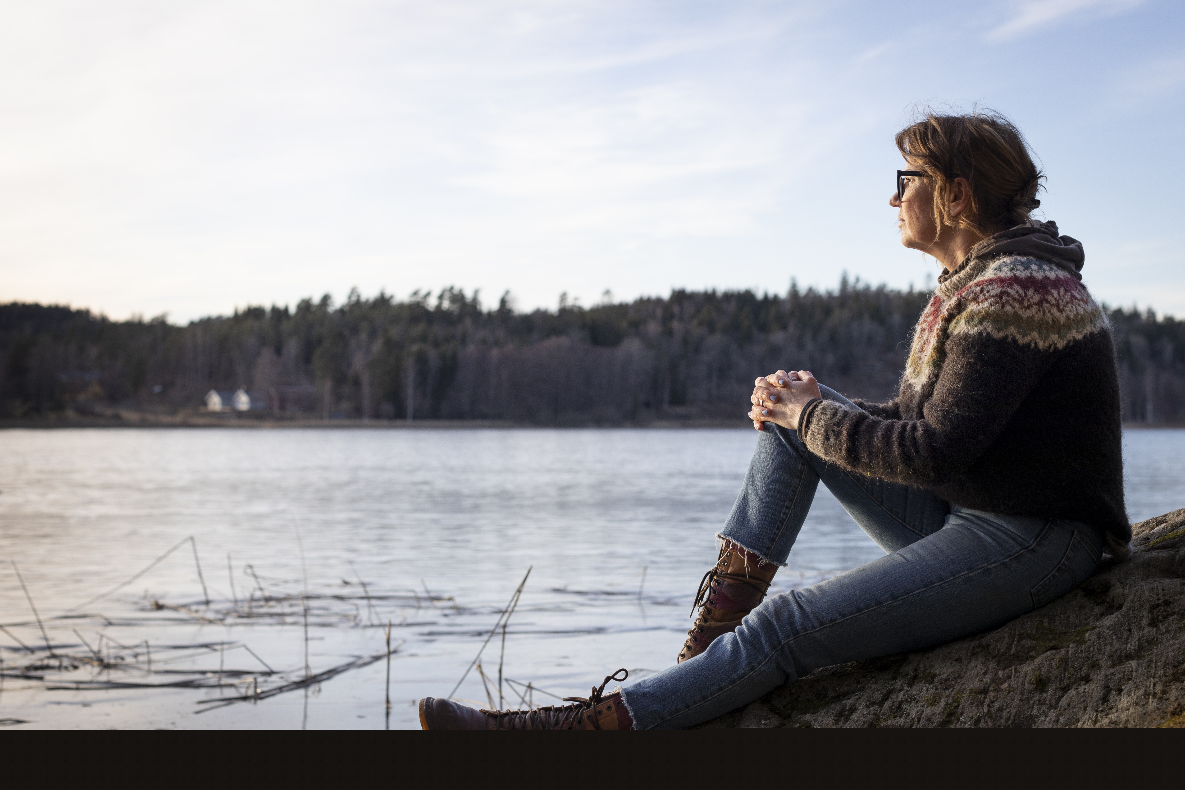 En kvinna sitter på en klippa och tittar ut över vattnet.