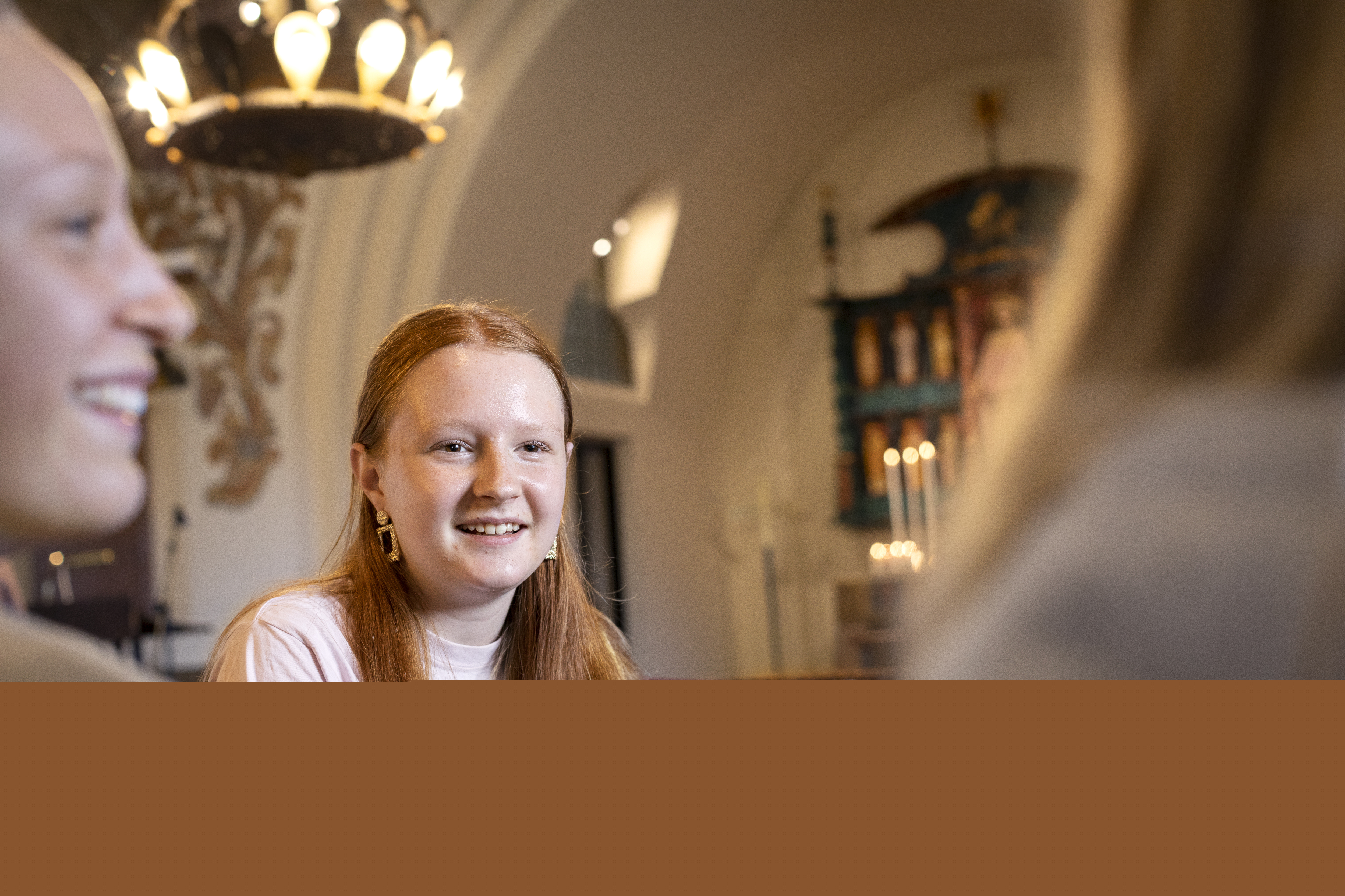 En rödhårig tonårstjej sitter i en kyrkbänk och snackar med några jämnåriga.