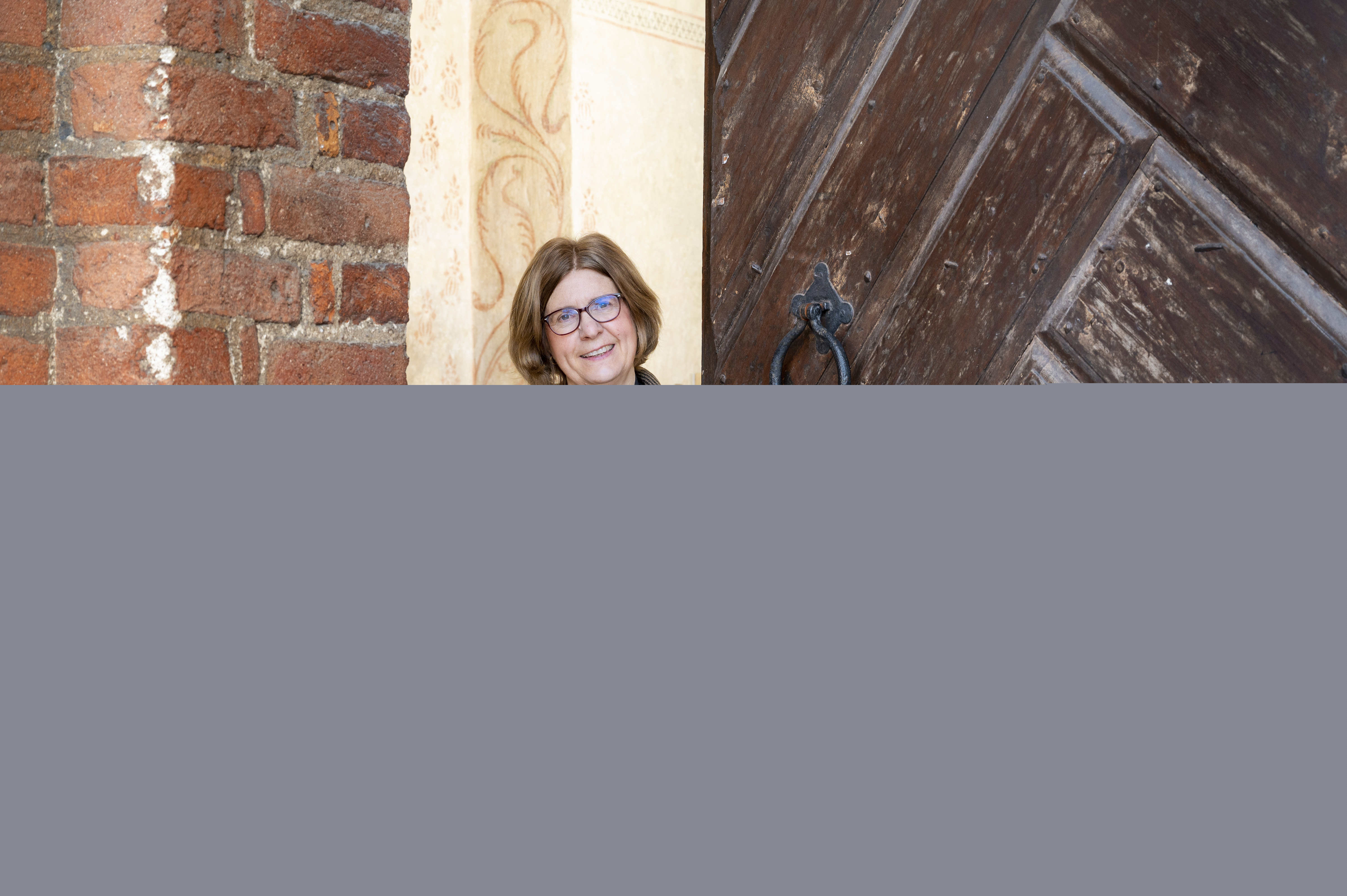 En kvinnlig präst står i dörröppningen till en tegelkyrka.