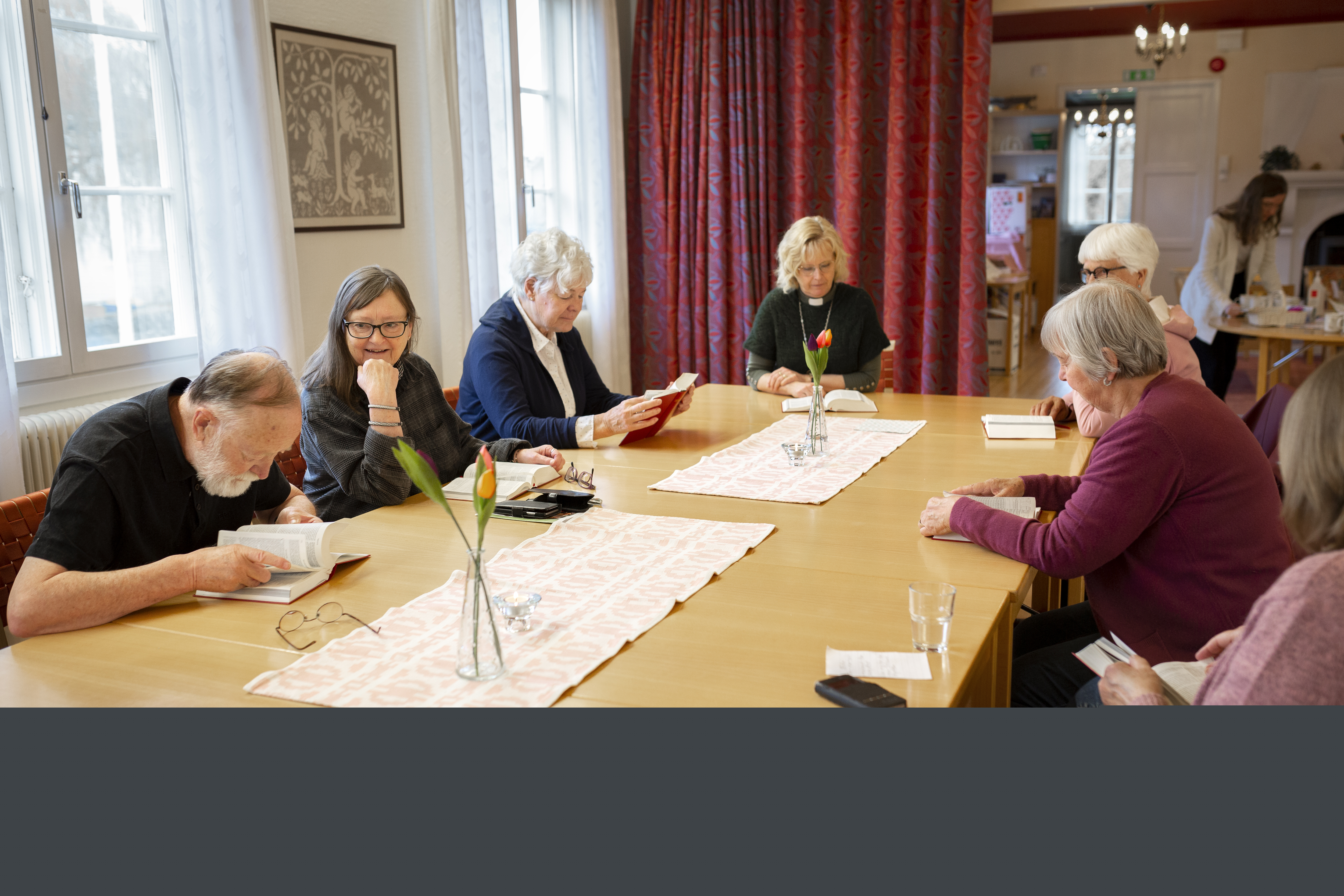 En grupp sitter runt ett mötesbord, alla med var sin bibel framför sig.