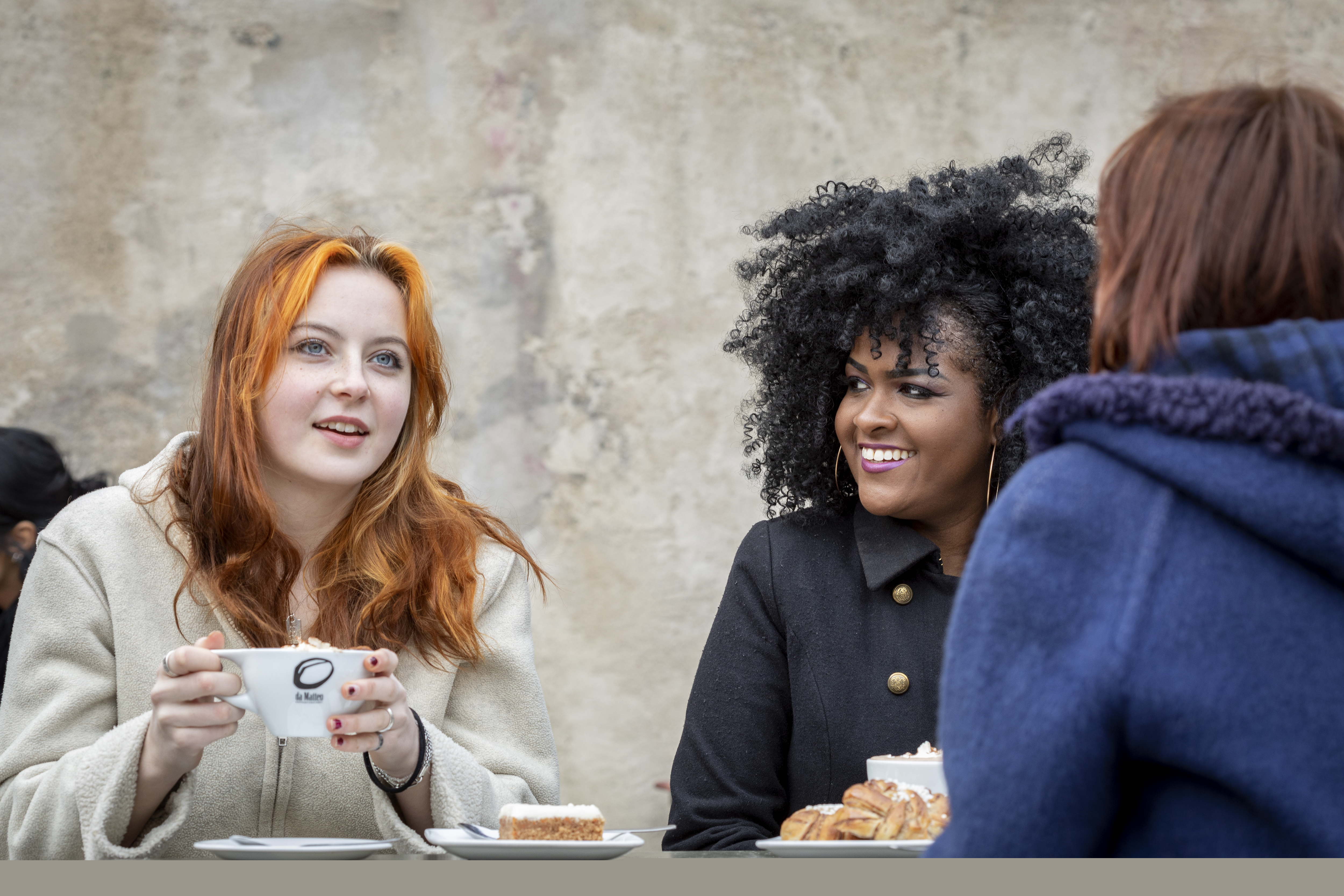 Några unga kvinnor sitter och fikar utomhus.