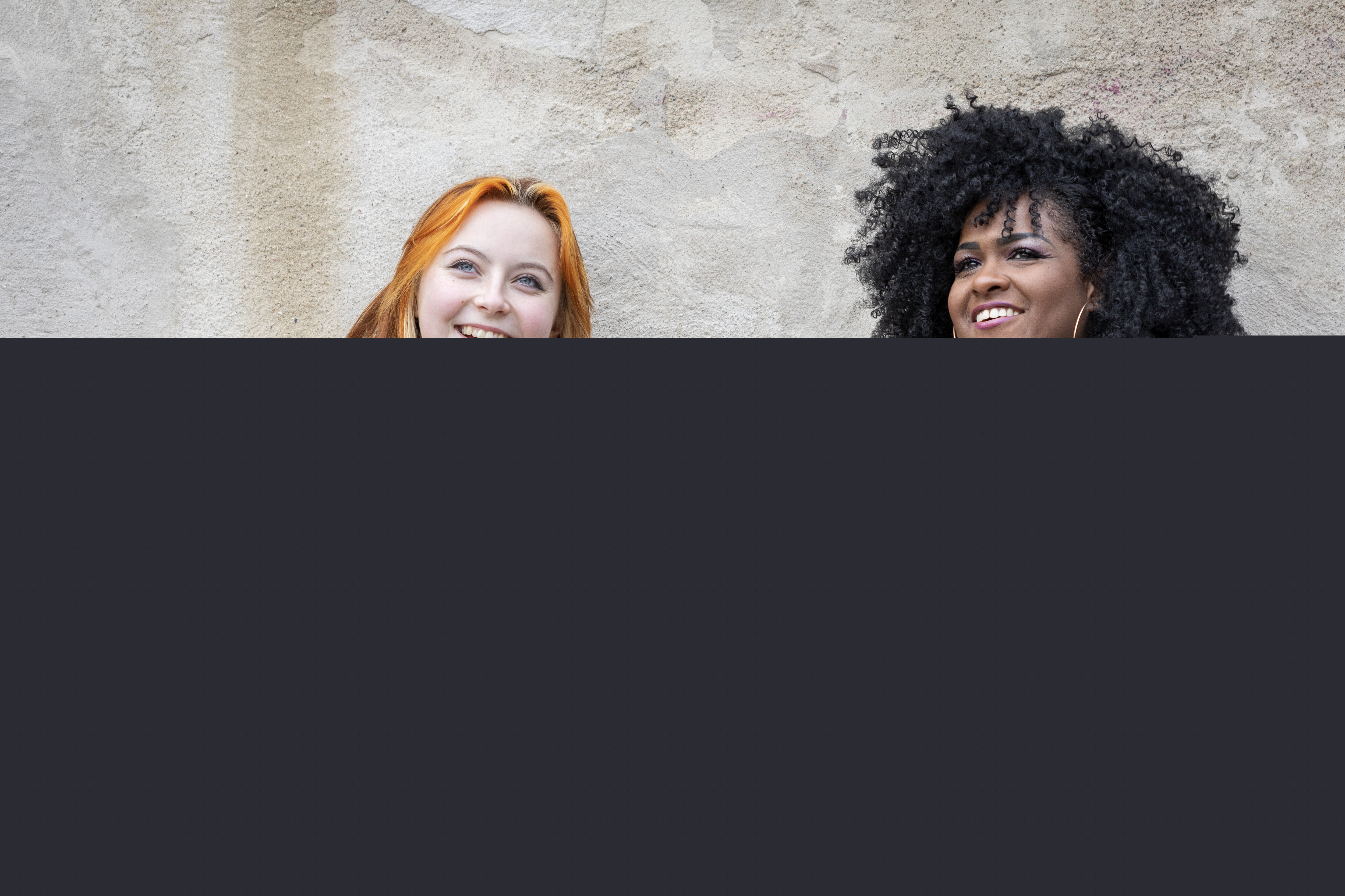 Två unga kvinnor sitter vid en putsad vägg.