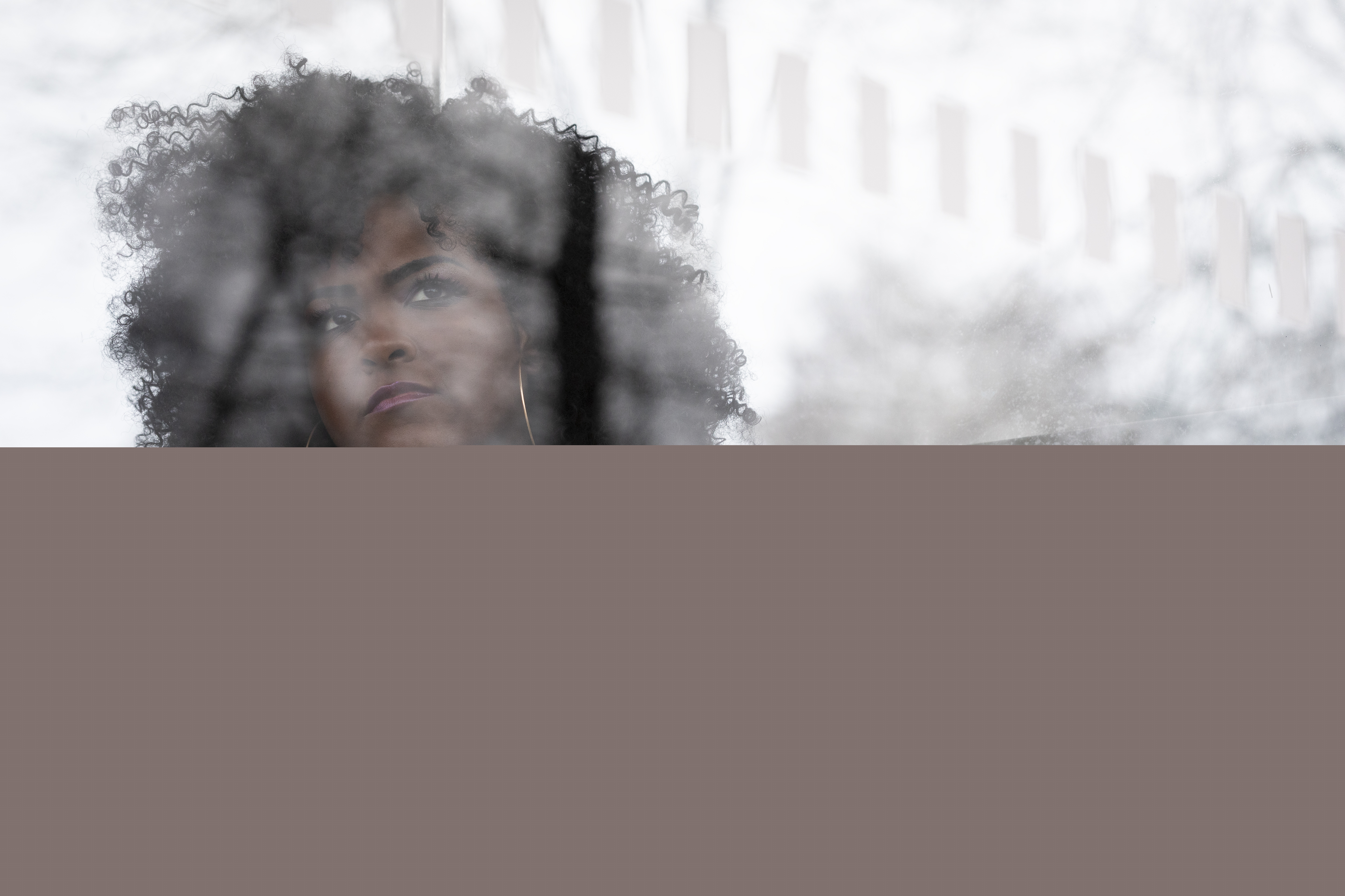 Bakom reflexerna i en busskurs glasruta syns en ung kvinna med svart lockigt hår.