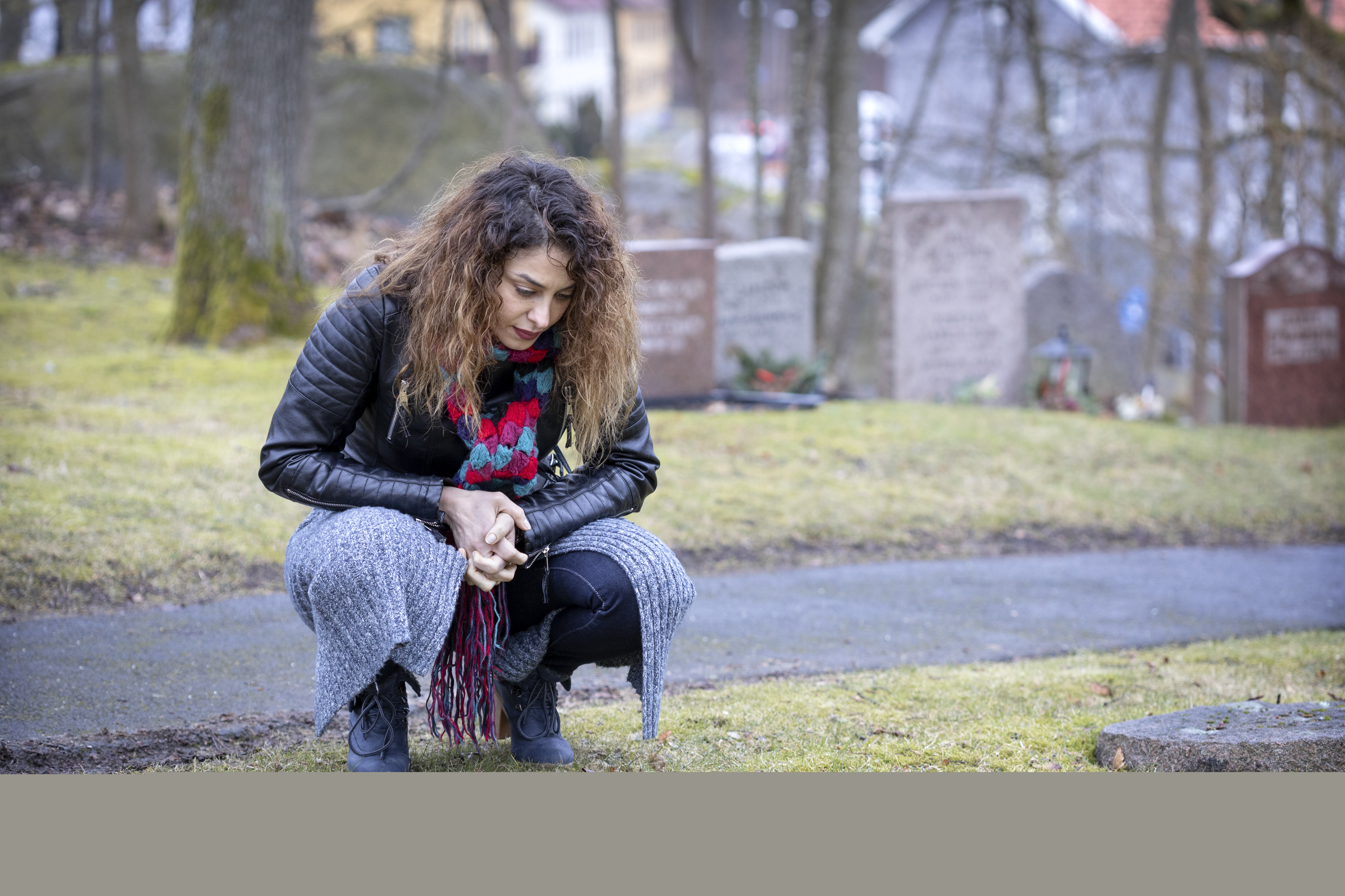 En kvinna på en kyrkogård sitter på huk vid en minnessten.