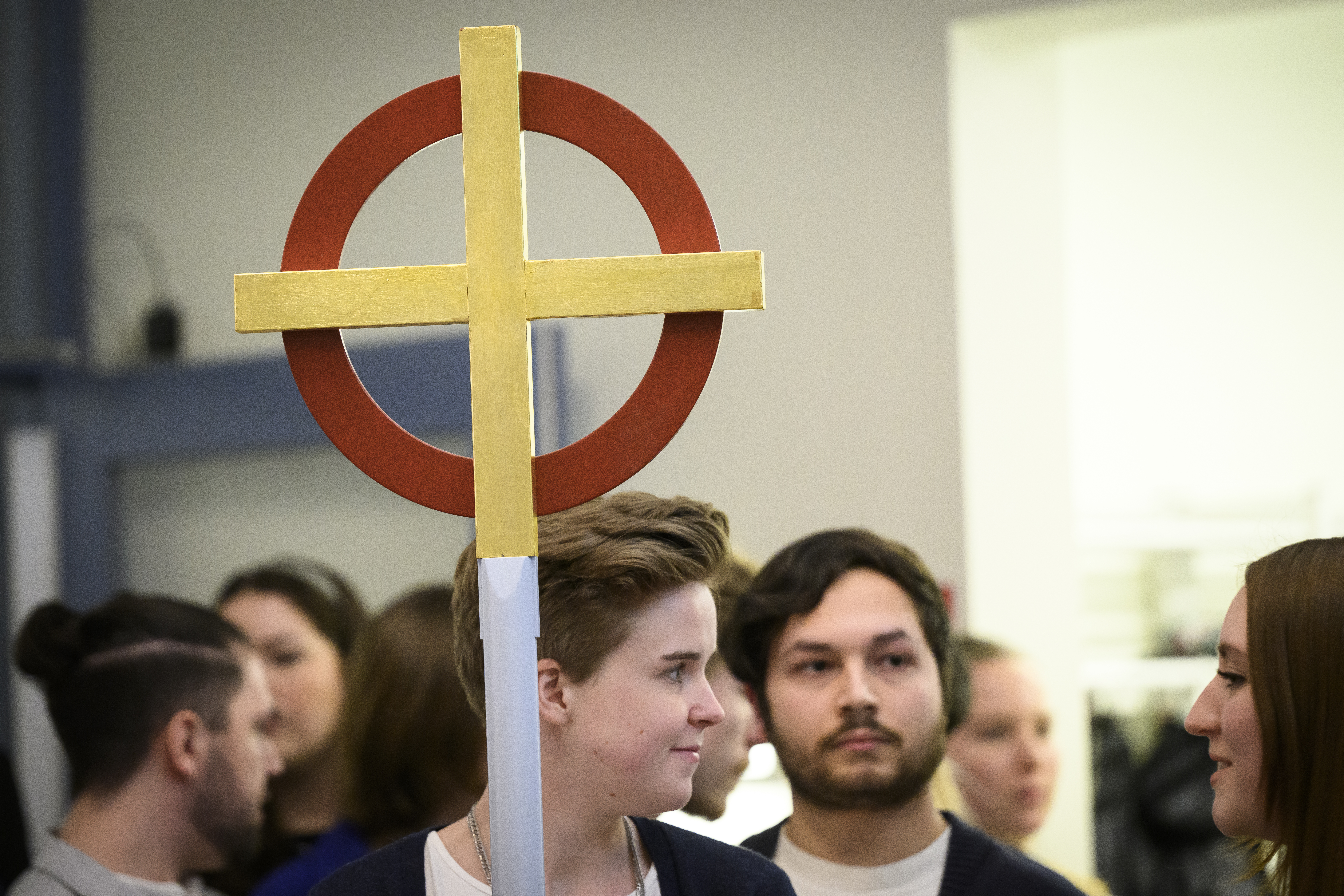 Några ungdomar förbereder sig för att gå in i kyrkan. En av dem håller ett processionskors.