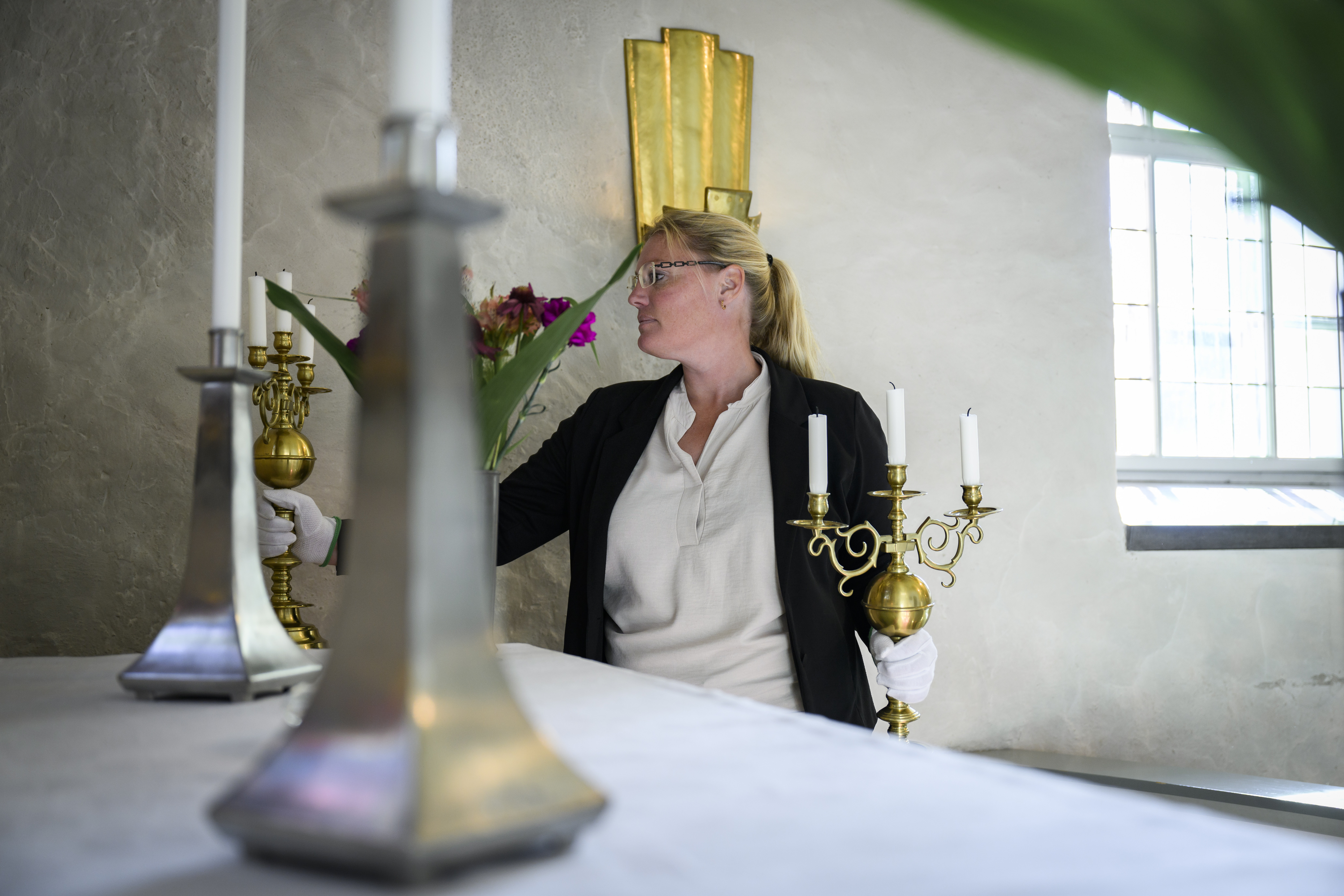 En kvinna med vita handskar ställer två stora mässingsljusstakar på ett altare i en kyrka.