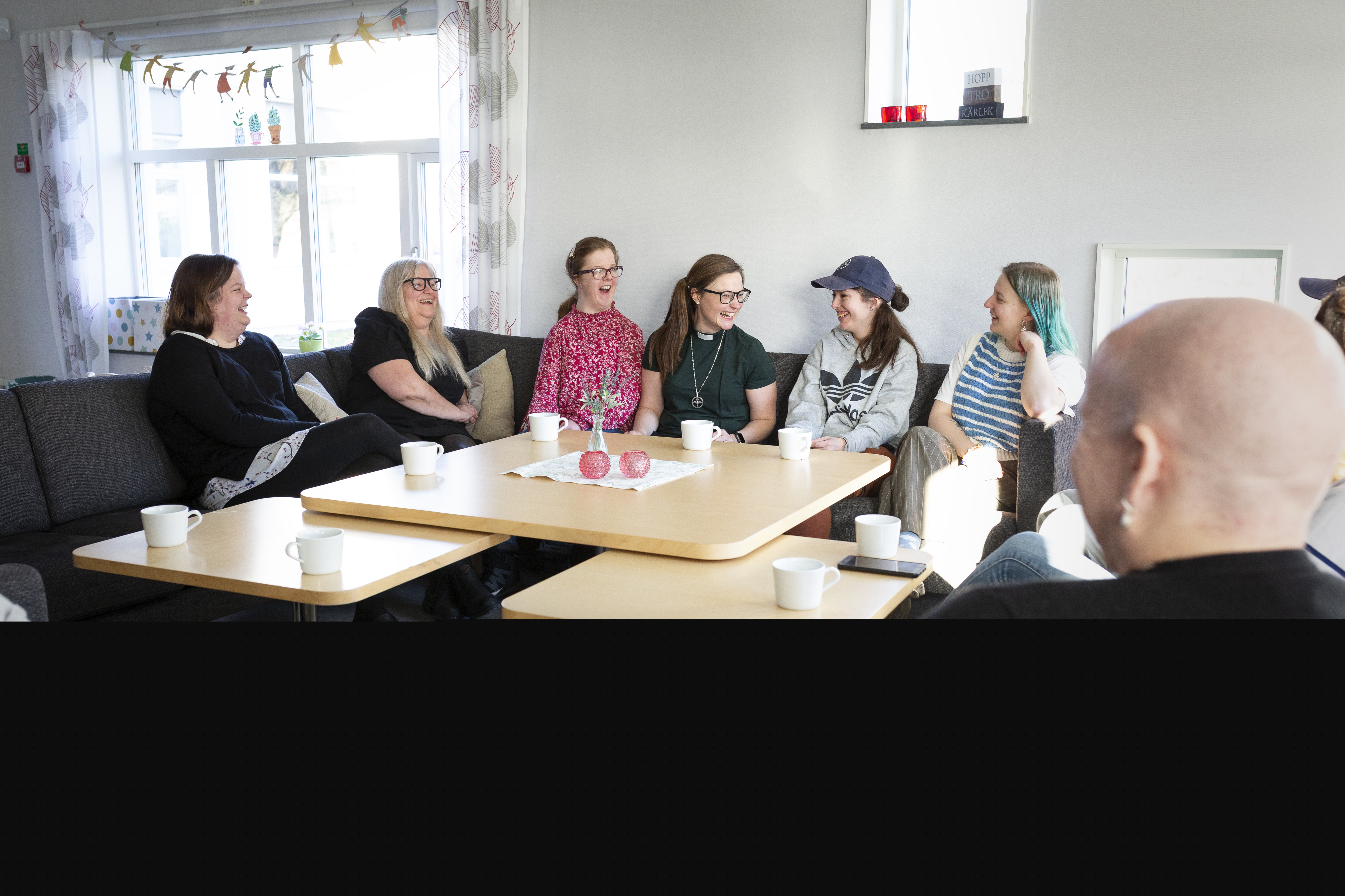 Ett gäng kvinnor i olika åldrar och en kvinnlig diakon sitter i en soffa och skrattar tillsammans.