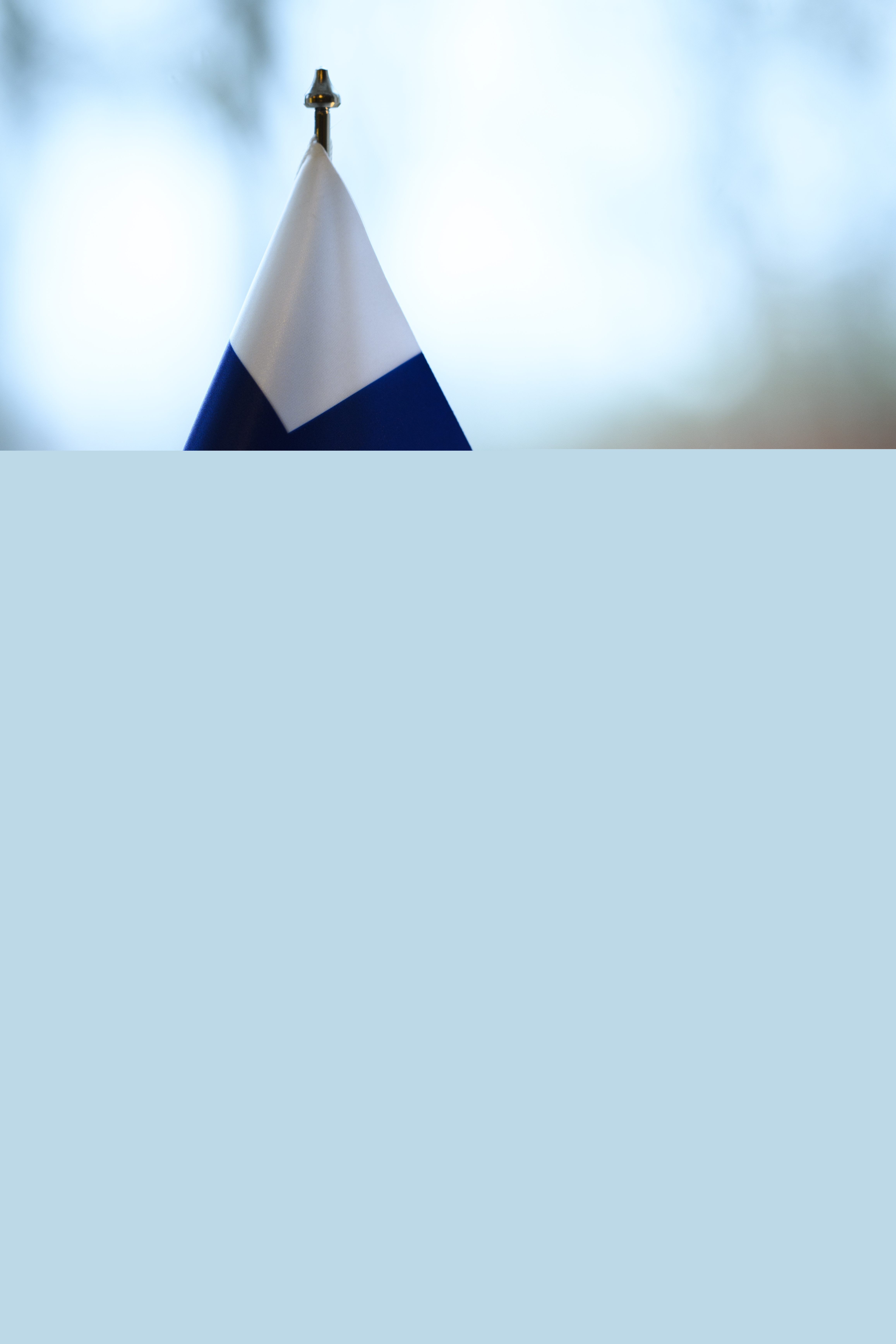 En finsk bordsflagga och ett brinnande stearinljus står i ett fönster.